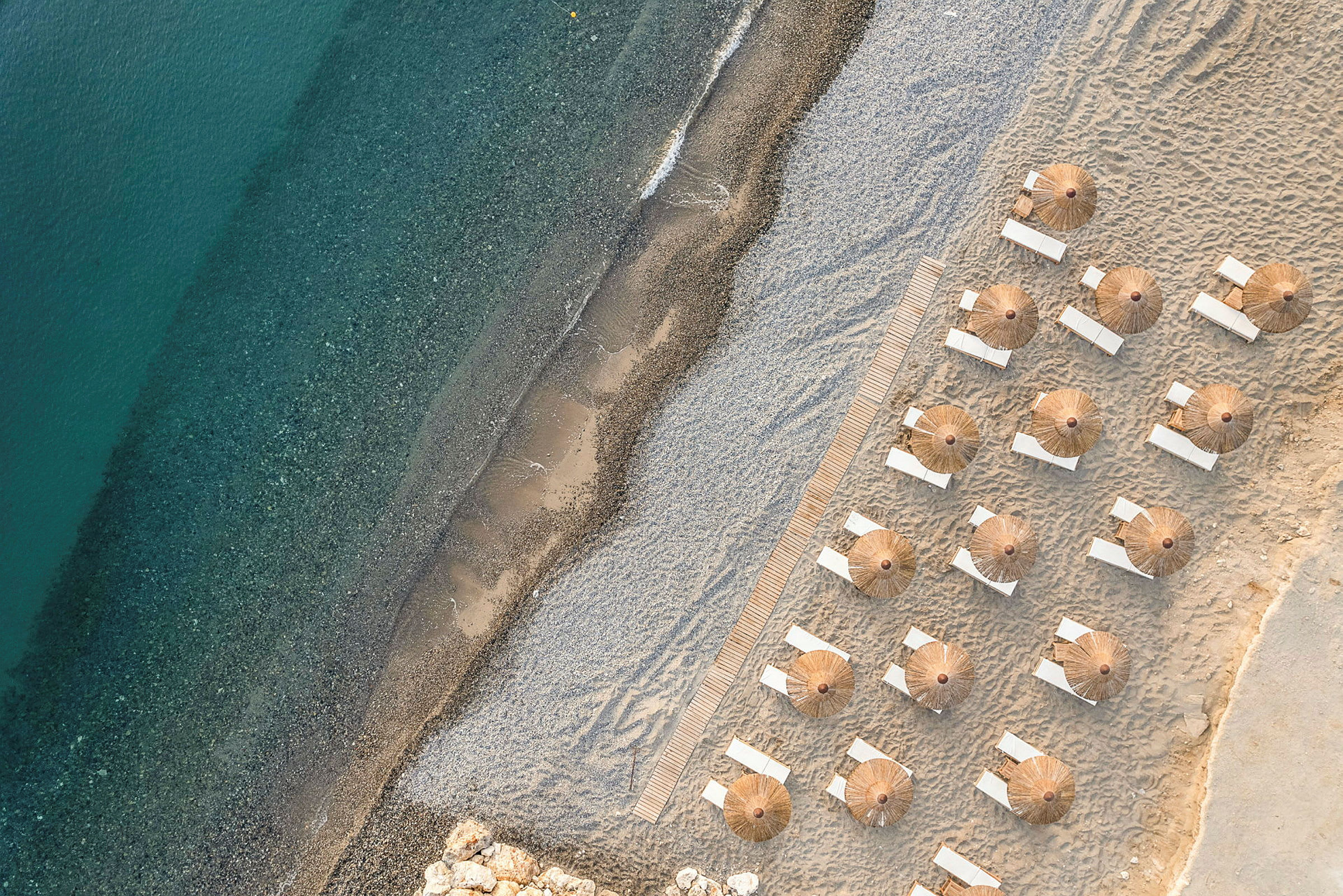 Bilde av en strand med blått vann og parasoller med solsenger i ordnede rekker. (AI-generert tekst)