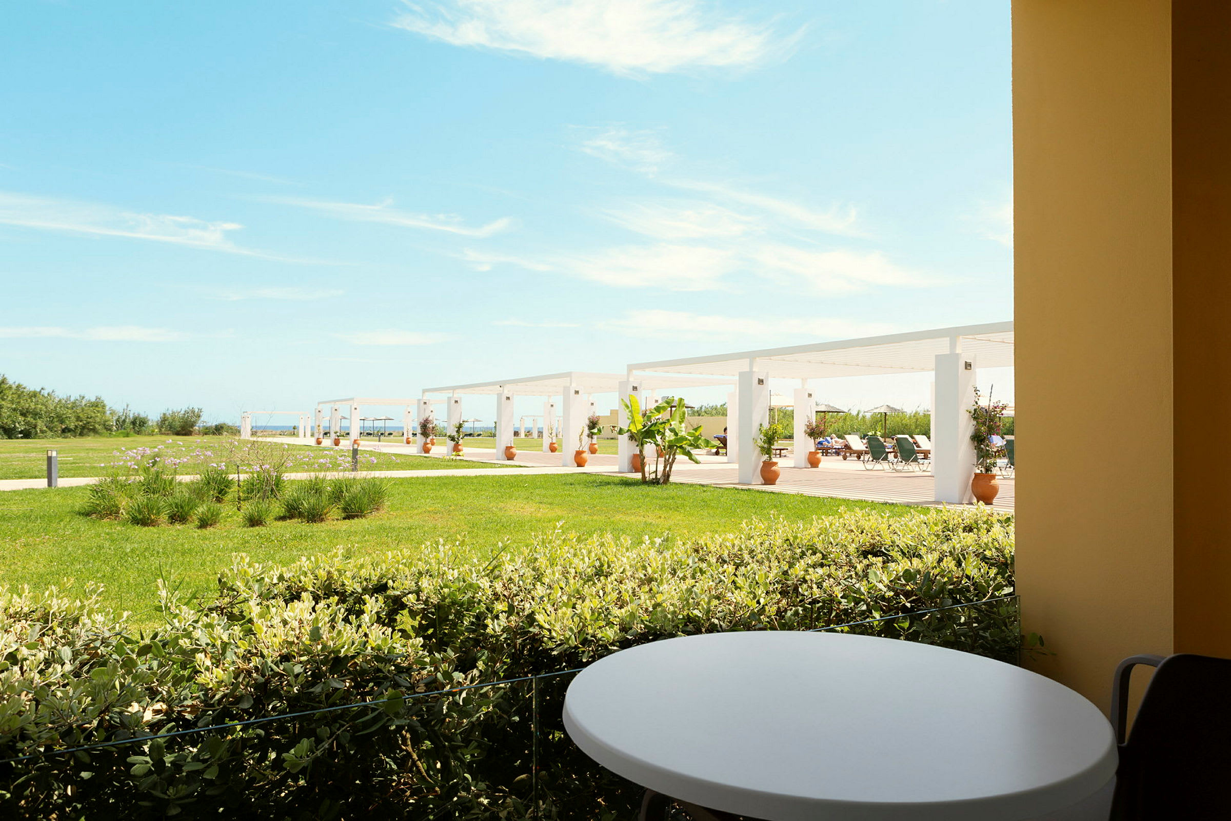 Utsikt fra en terrasse med et rundt bord mot en plen og pergola i bakgrunnen. (AI-generert tekst)
