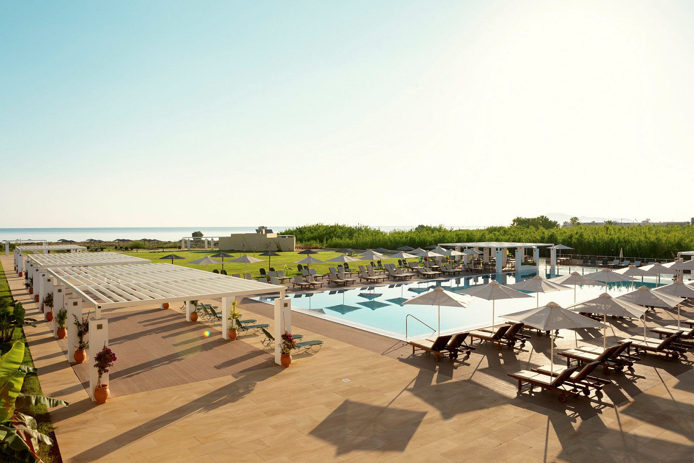 Et utendørs svømmebasseng med solsenger og parasoller på et hotellområde nær havet. (AI-generert tekst)