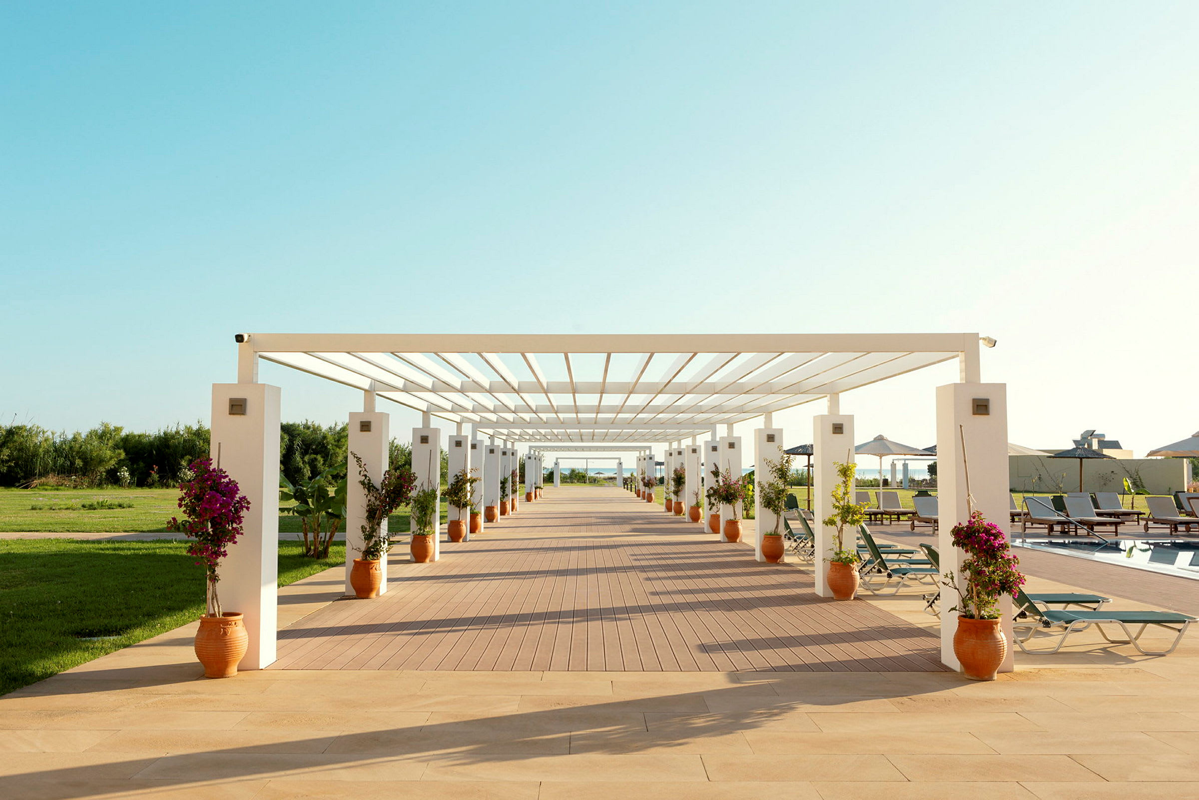 Åpen trepergola omgitt av blomsterpotter og solsenger ved et basseng. (AI-generert tekst)