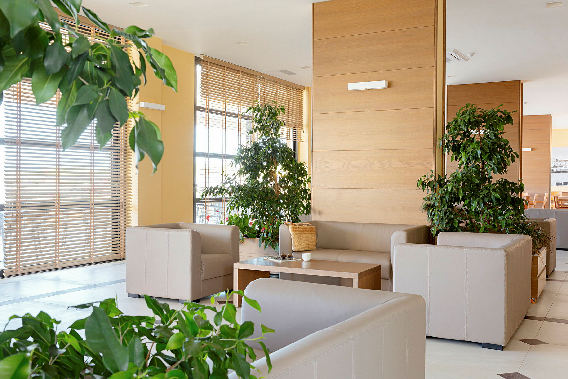 Bilde av en moderne og lys stue med beige sofaer, et trebord og grønne planter. (AI-generert tekst)