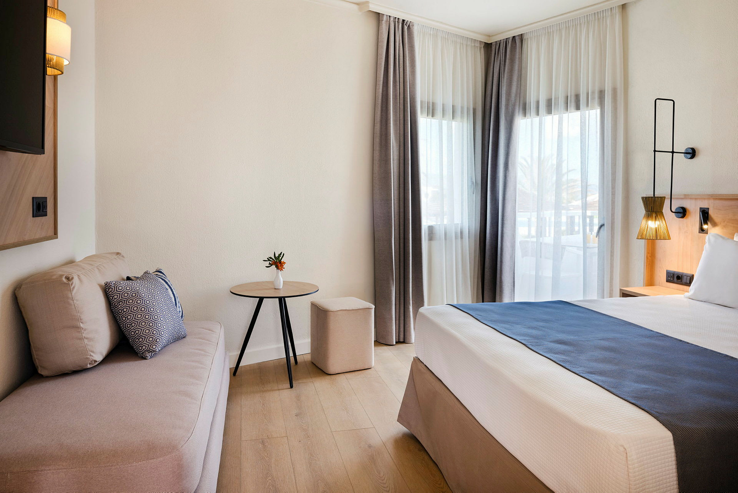 Et hotellrom med en seng, sofa og bord ved siden av store vinduer. (AI-generert tekst)