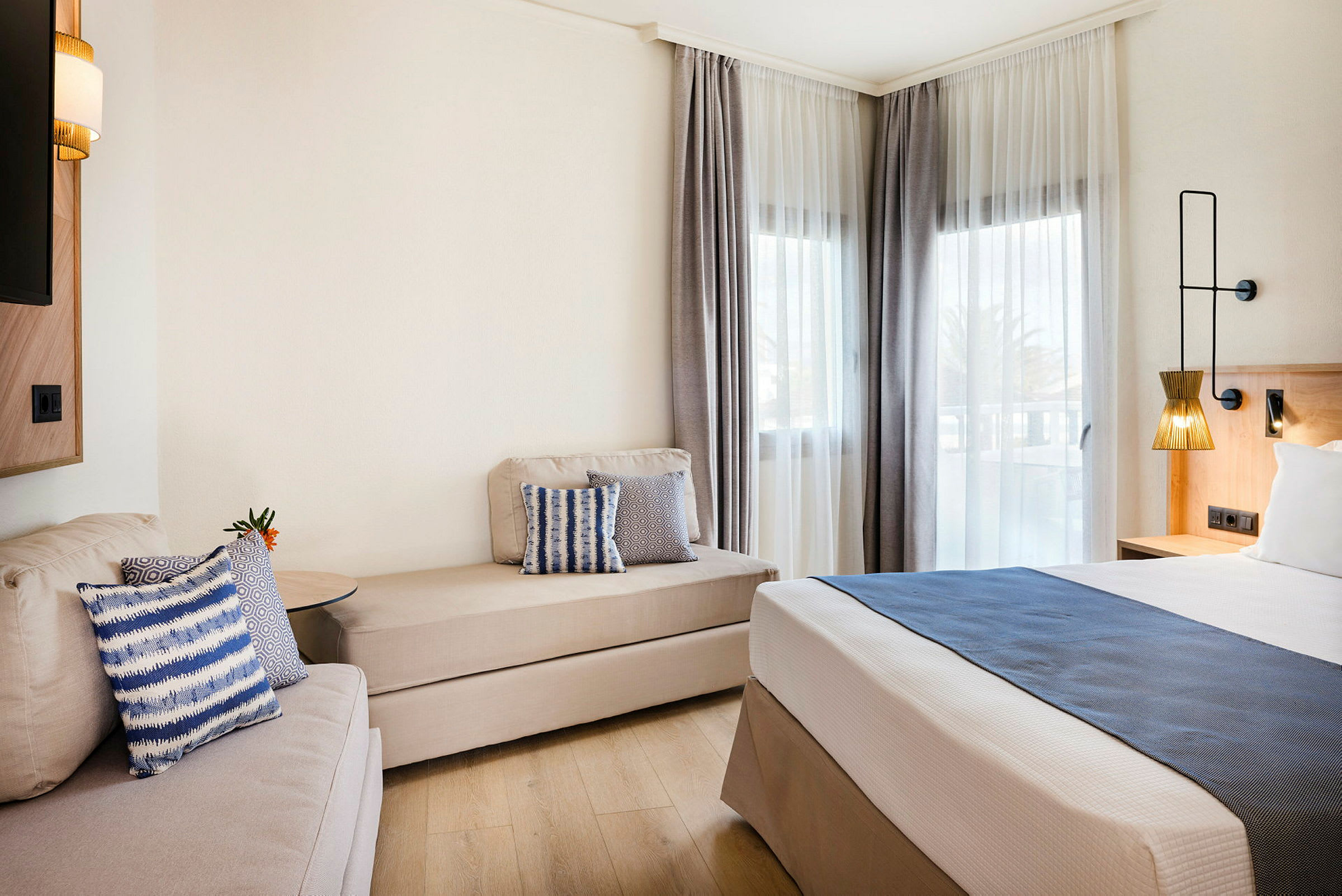Moderne hotellrom med seng, sofa og vinduer med lyse gardiner. (AI-generert tekst)