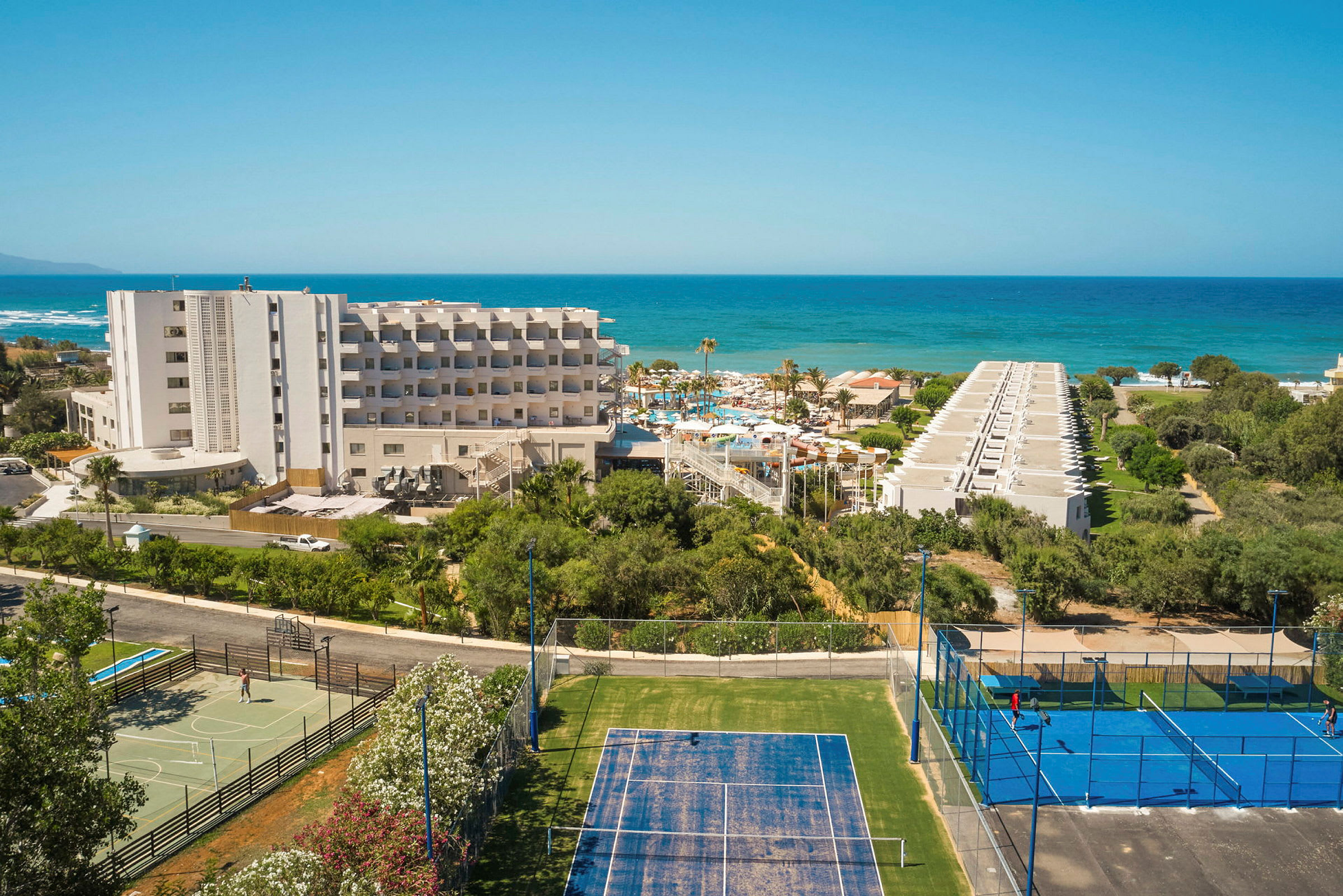 Hotellbygning med tennisbaner i forgrunnen og havet i bakgrunnen. (AI-generert tekst)