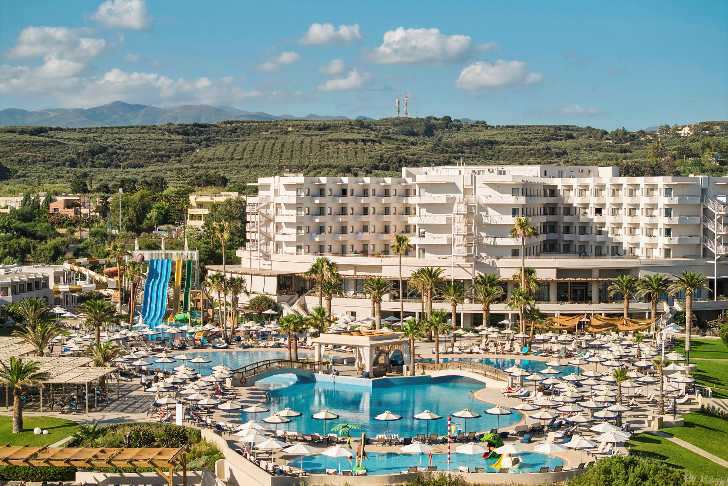 Resort med et stort bassengområde og vannsklier, omgitt av grøntområder. (AI-generert tekst)