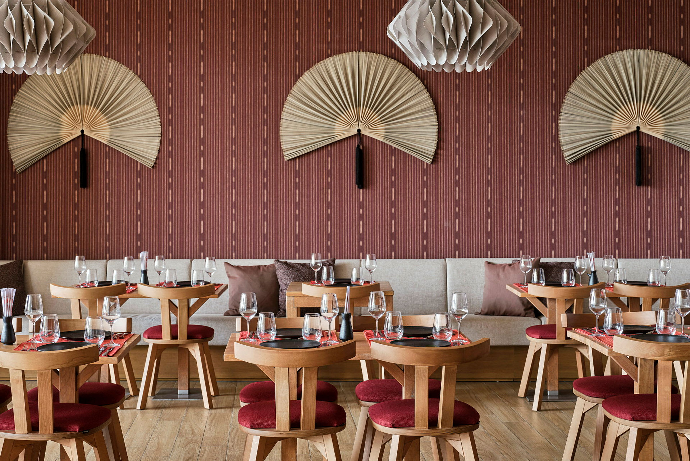 En restaurant med trebord og røde stoler, dekorert med vegghengte vifter og moderne lamper. (AI-generert tekst)