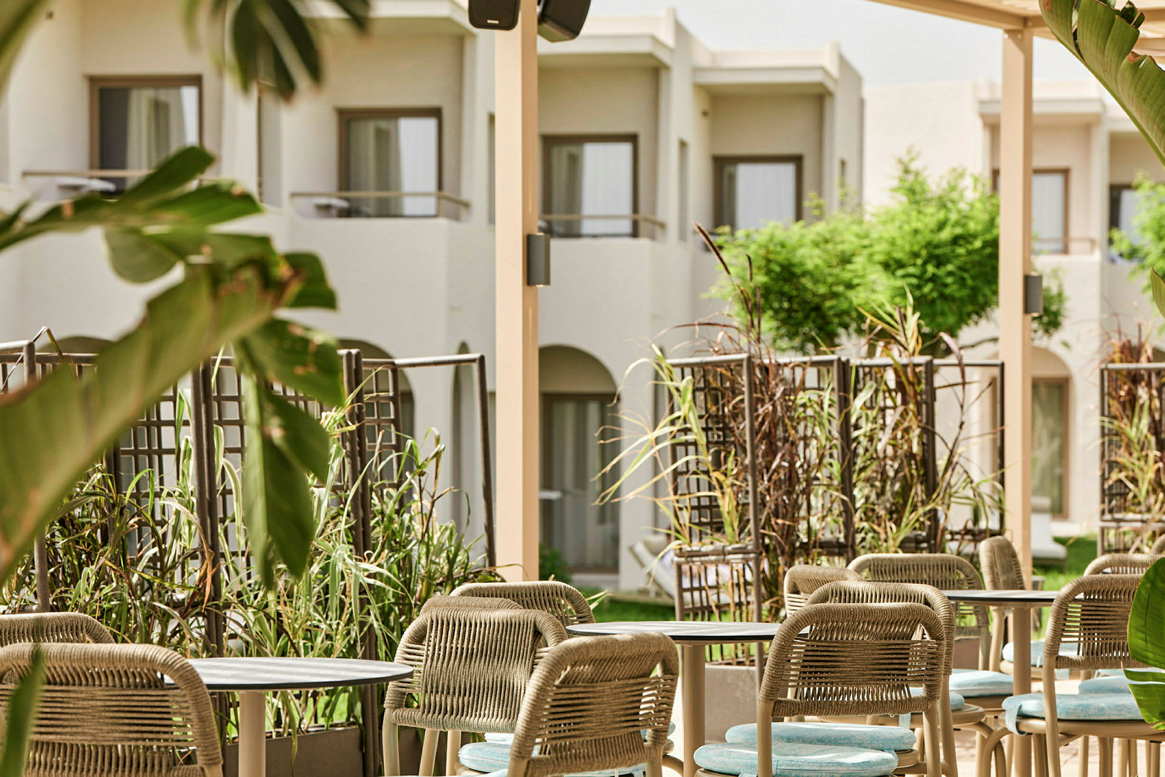 Bilde av en hotellhage med sittegruppe og grønne planter, hvit fasade i bakgrunnen. (AI-generert tekst)