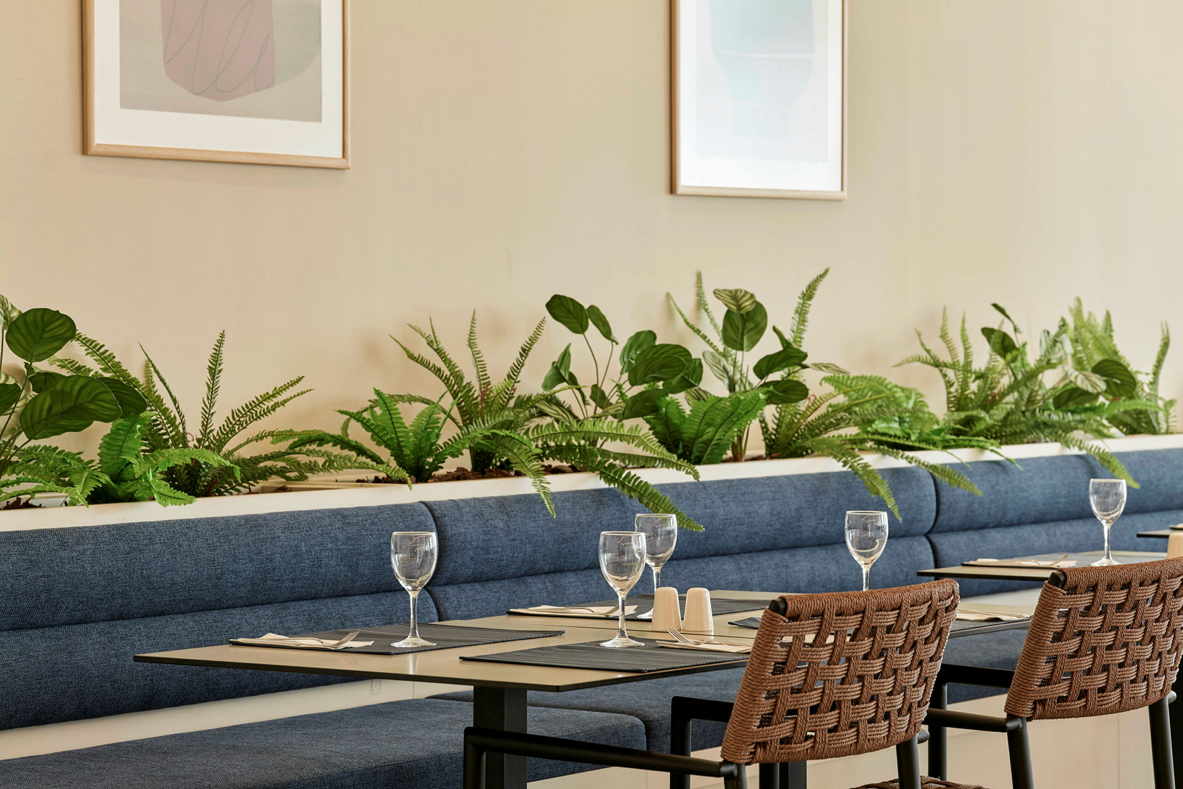 Et restaurantområde med blå sofaer, dekorert med grønne planter og bord dekket. (AI-generert tekst)