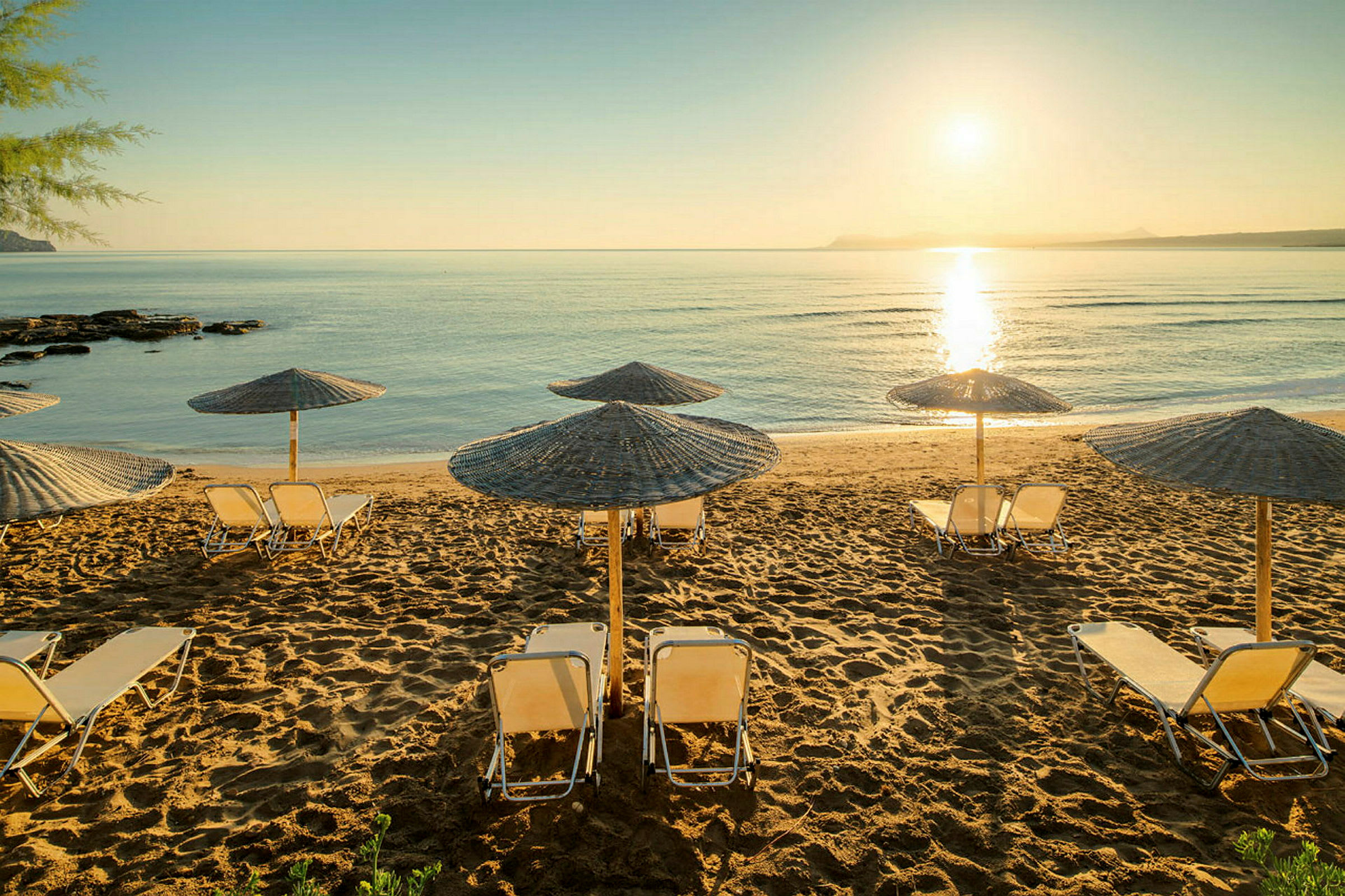 Solstoler med parasoller på en sandstrand ved havet i solnedgang. (AI-generert tekst)