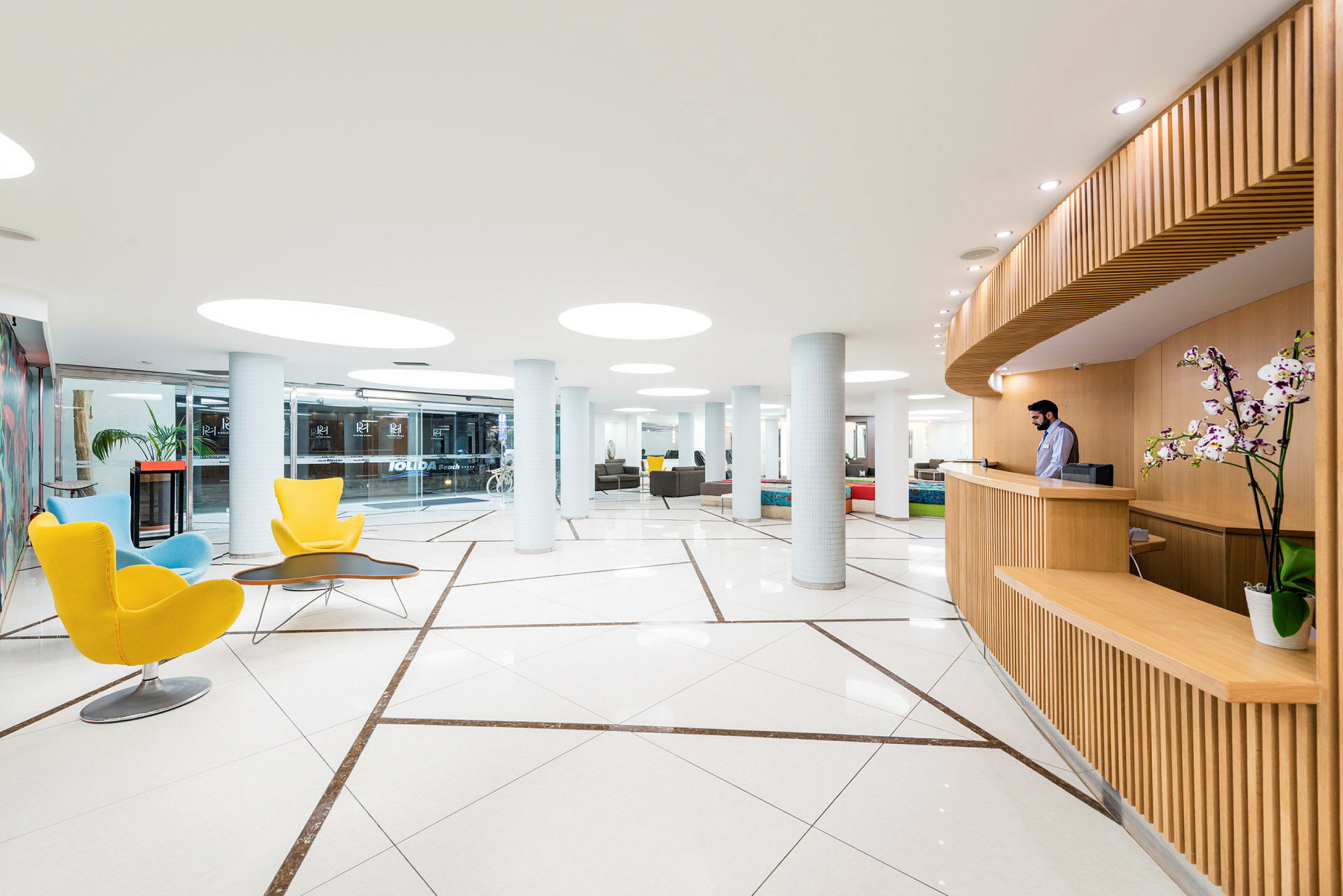 Moderne hotellobby med lyse møbler, tredetaljer og glasstak. (AI-generert tekst)