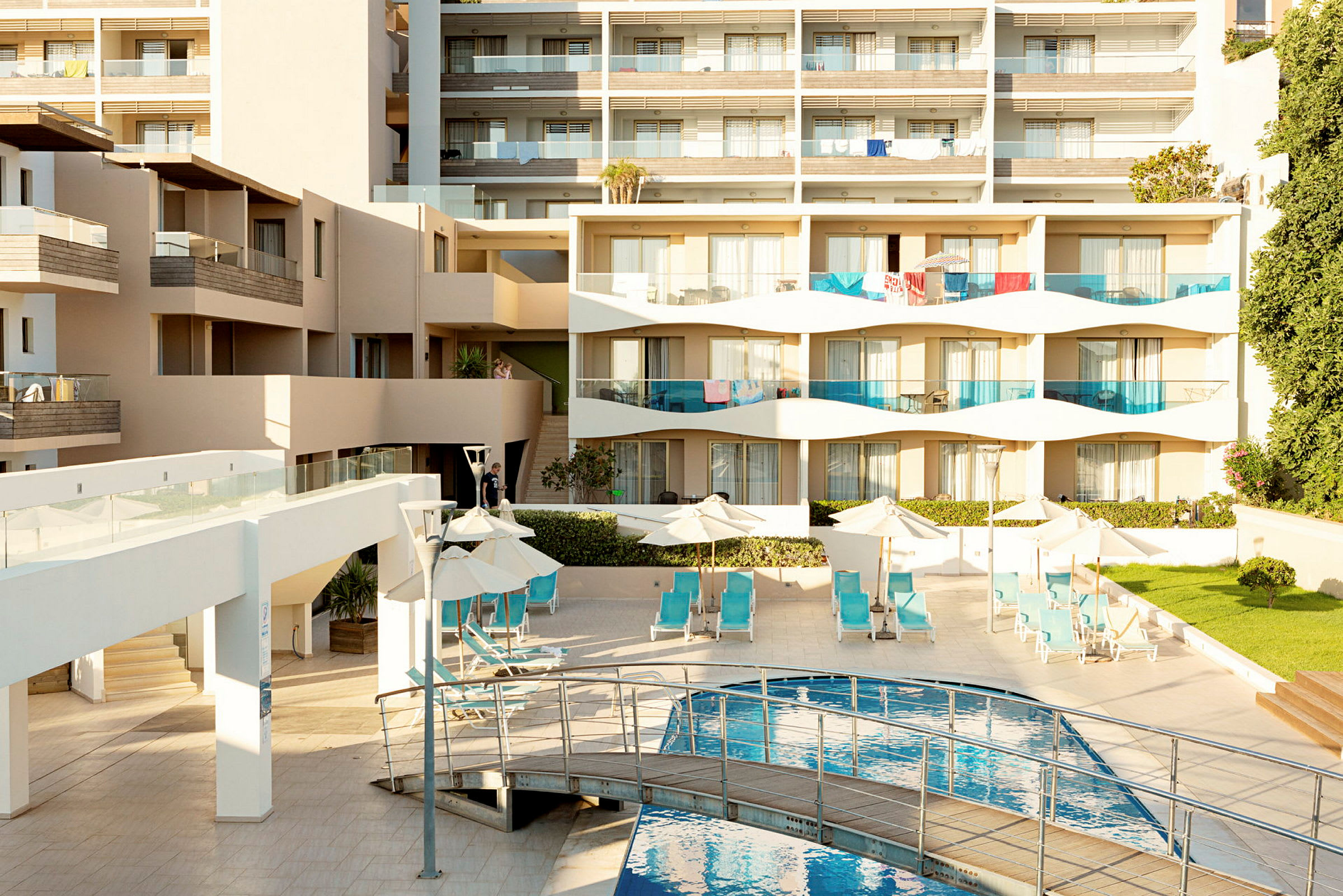 En moderne hotellbygning med balkonger, solsenger ved et basseng og grøntarealer. (AI-generert tekst)