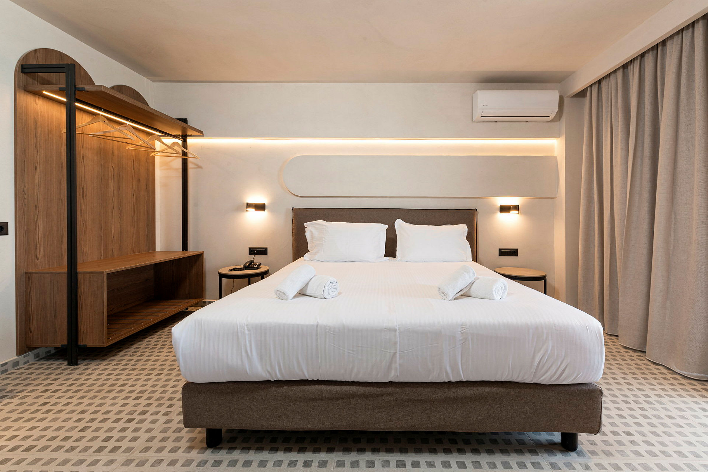 Et hotellrom med en dobbeltseng ved siden av et sidebord og en åpen garderobe. (AI-generert tekst)