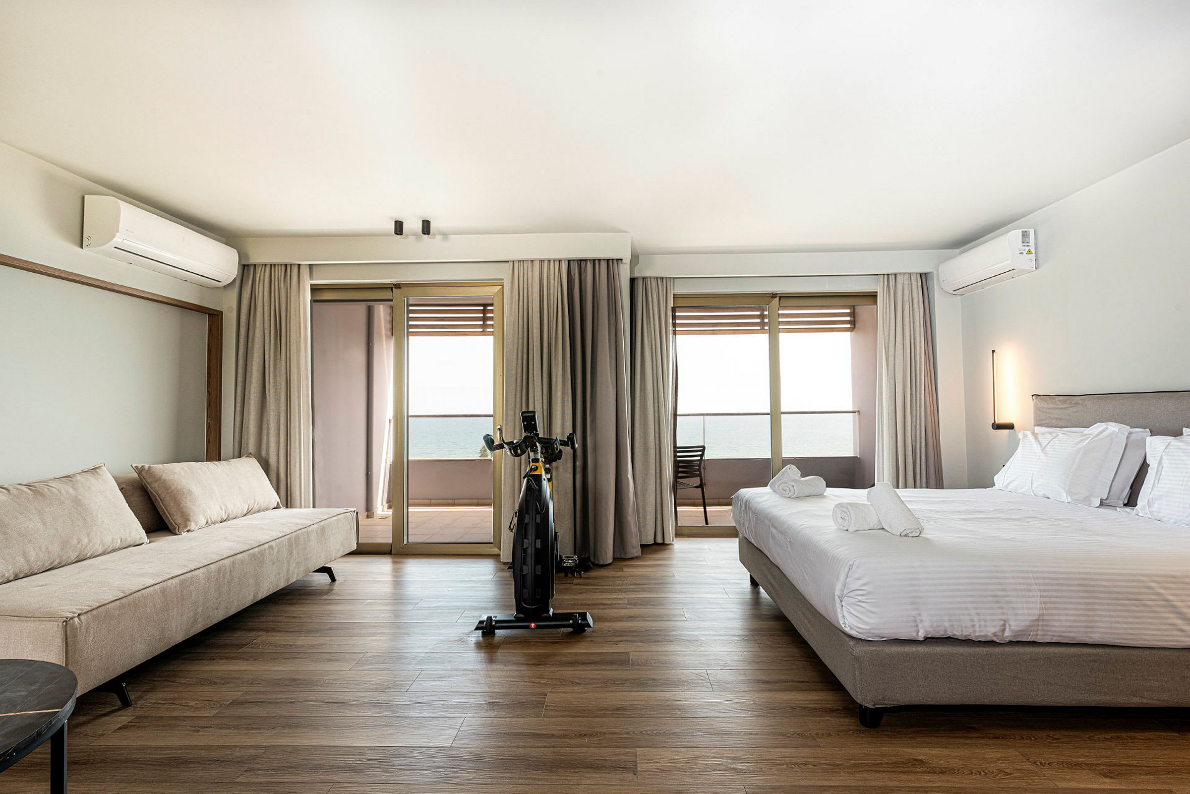 Et hotellrom med en seng og en sofa, utsikt mot en balkong og havet. (AI-generert tekst)