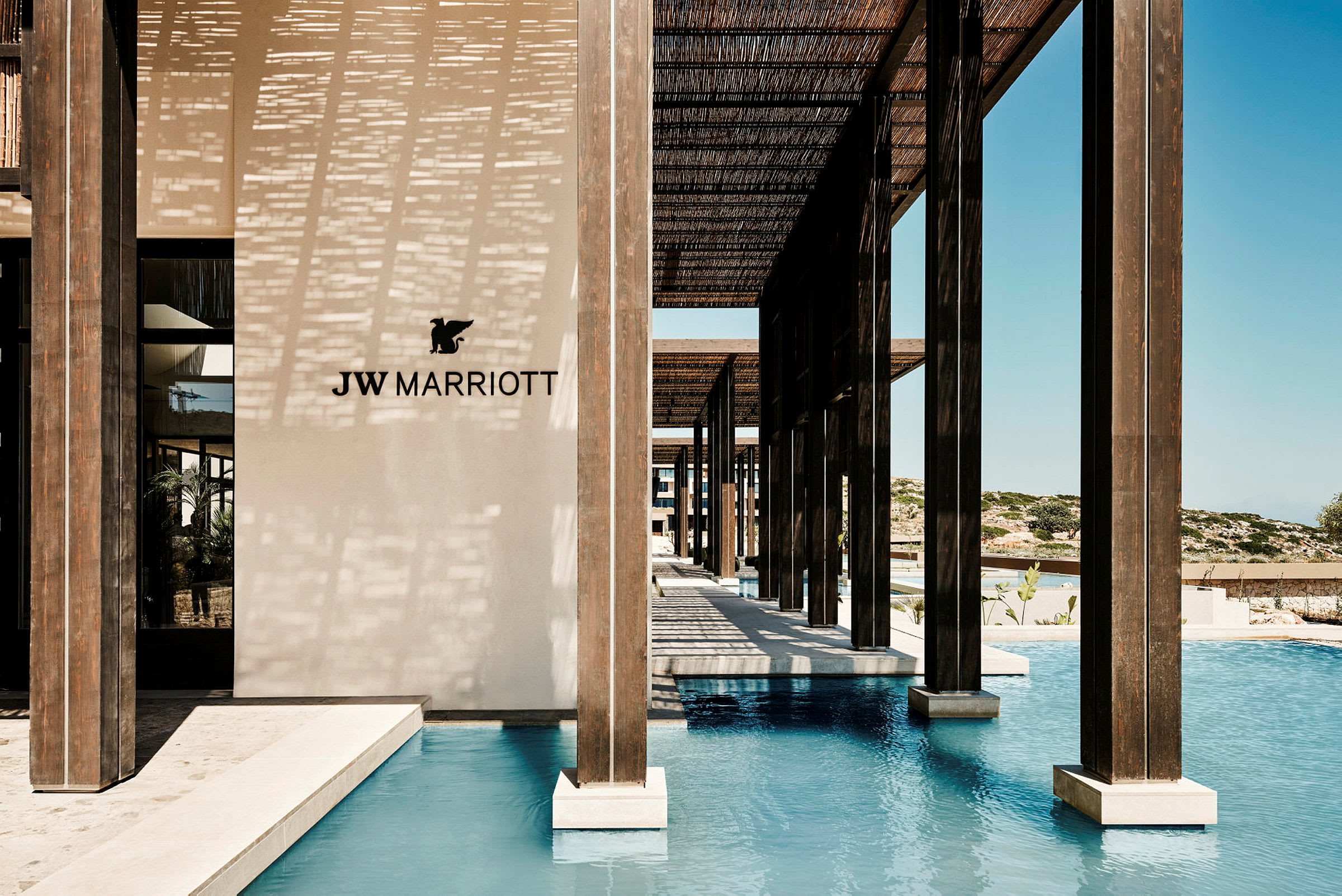 JW Marriott-logo på en lys vegg ved et basseng med trestolper. (AI-generert tekst)