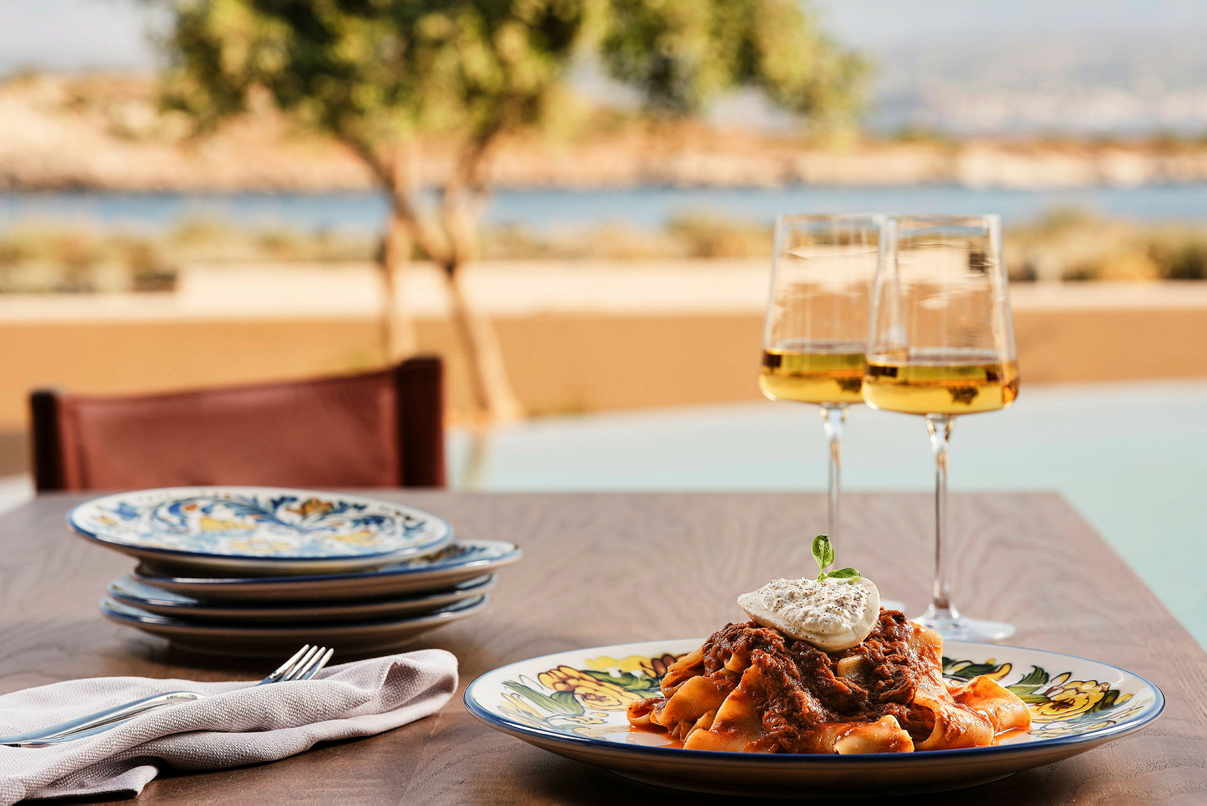 En tallerken med pasta og et glass hvitvin på et bord med utsikt mot naturen. (AI-generert tekst)