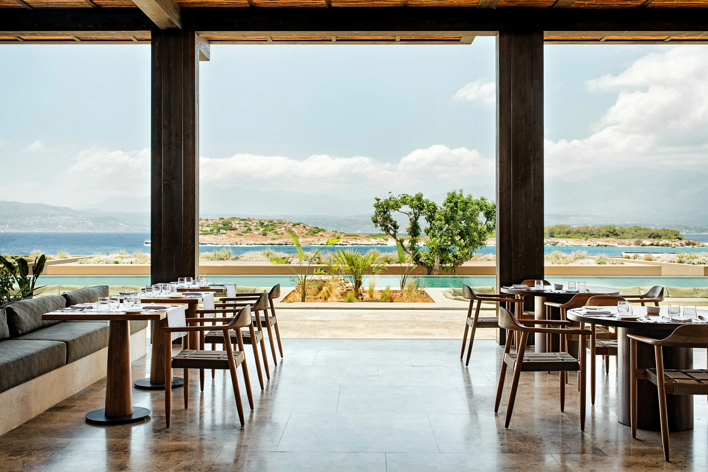 En restaurant med bord og stoler, med utsikt over havet og omgivelsene. (AI-generert tekst)