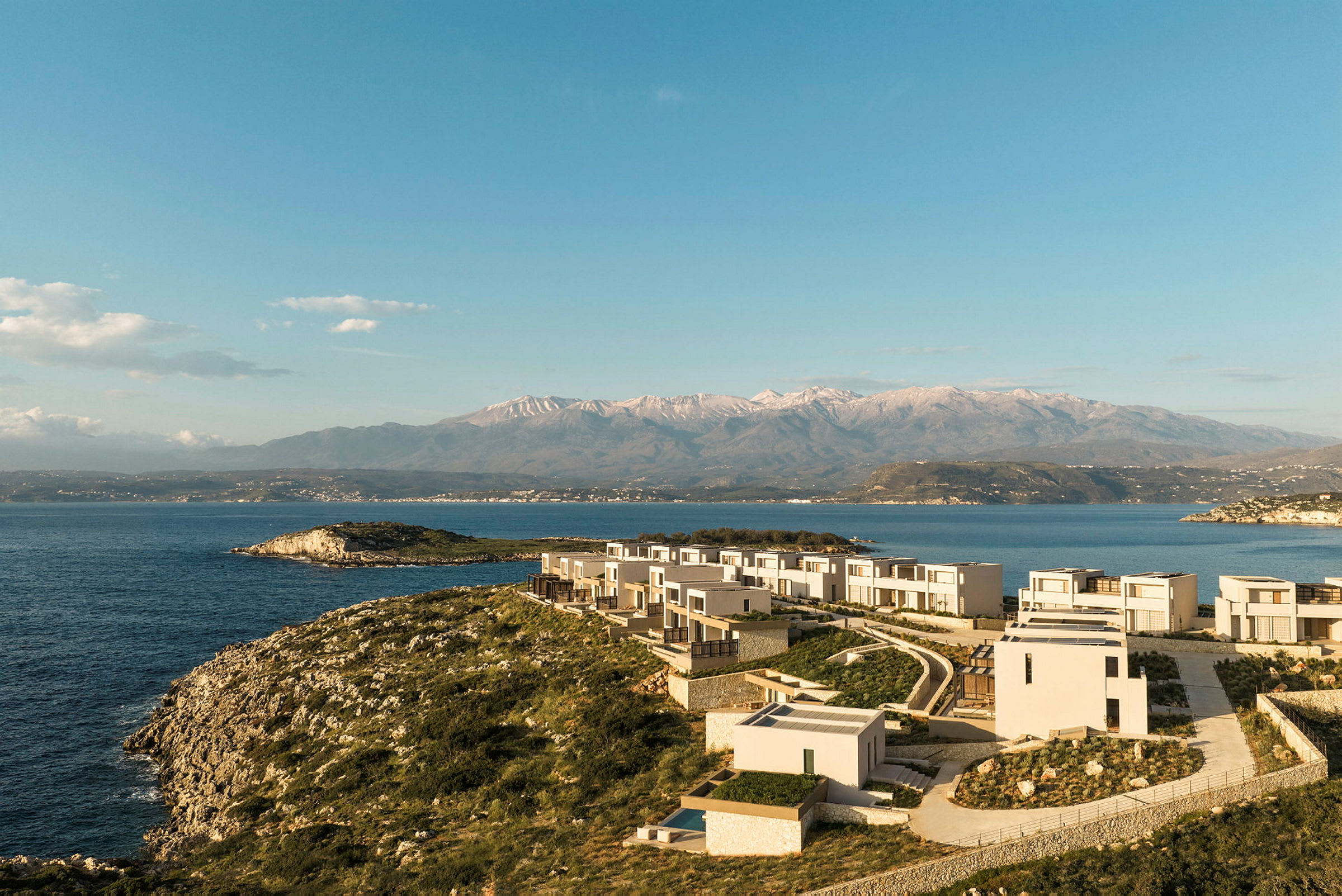 En kystlinje med moderne arkitektur nær havet og fjell i bakgrunnen. (AI-generert tekst)