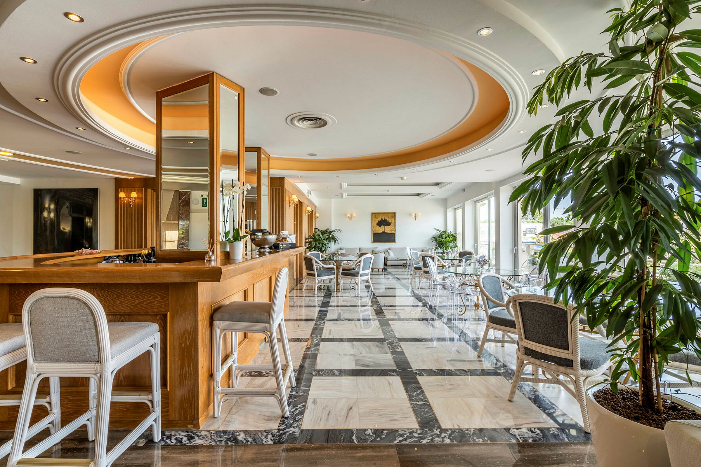 Et elegant hotellrom med tremøbler og marmorgulv, store vinduer, samt planter og sittemøbler. (AI-generert tekst)