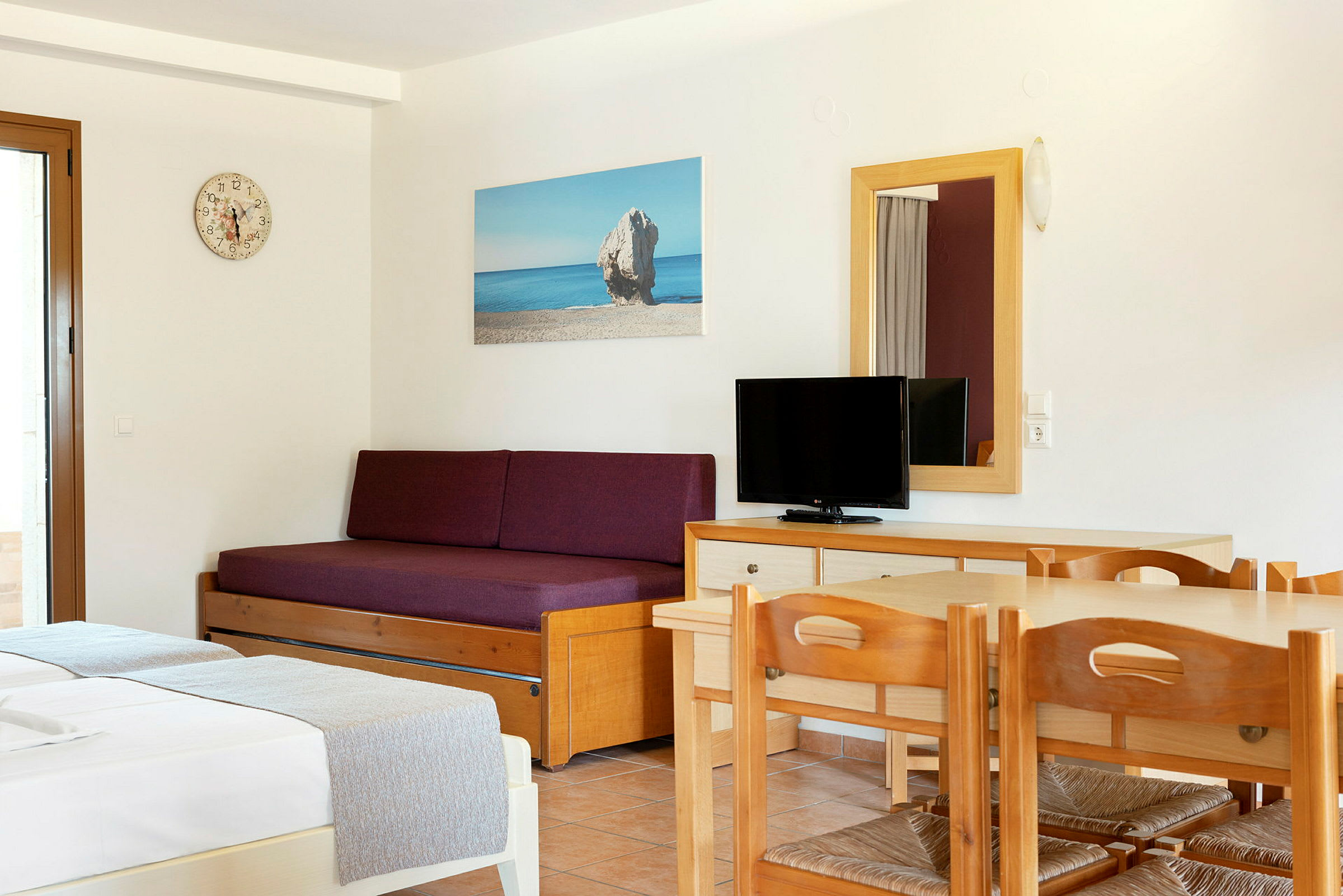 Innredning av et hotellrom med en sovesofa, et bord med stoler og en TV. (AI-generert tekst)