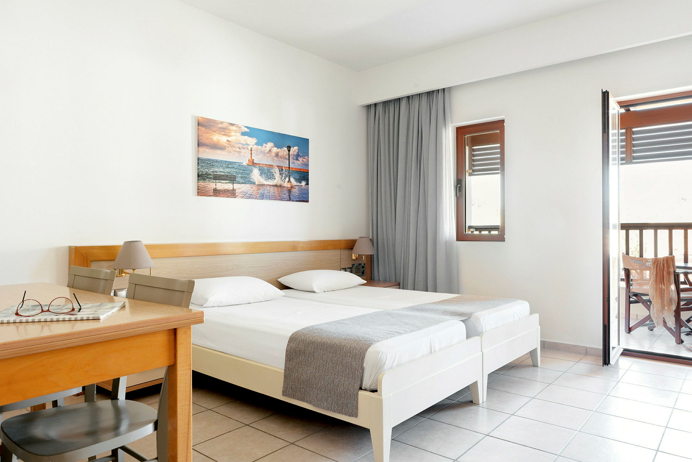 Hotellrom med to enkeltsenger, et trebord og stol samt balkong. (AI-generert tekst)