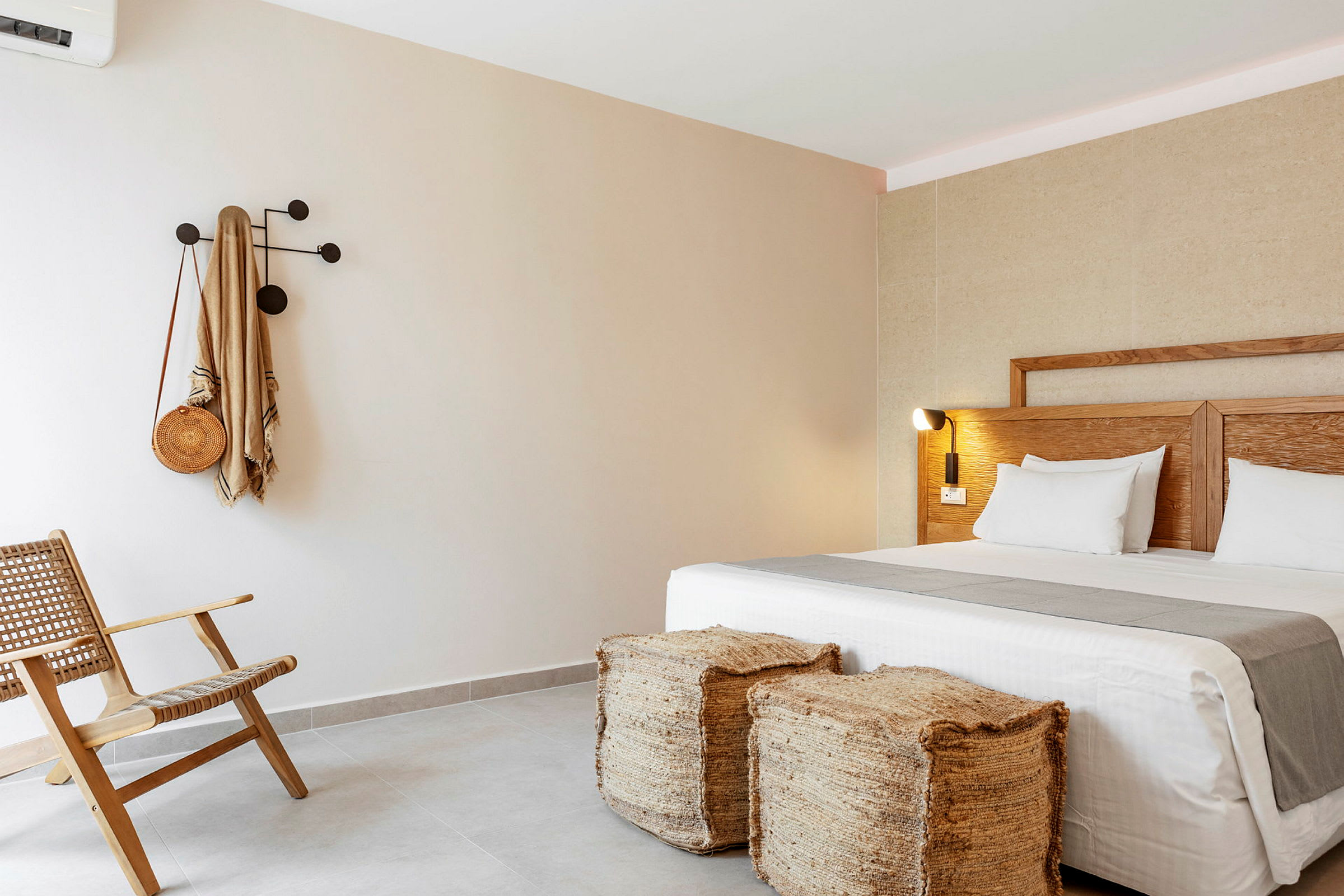 Hotellrom med moderne interiør som inkluderer en seng, to avføringskrakker, en stol og en krok på veggen. (AI-generert tekst)