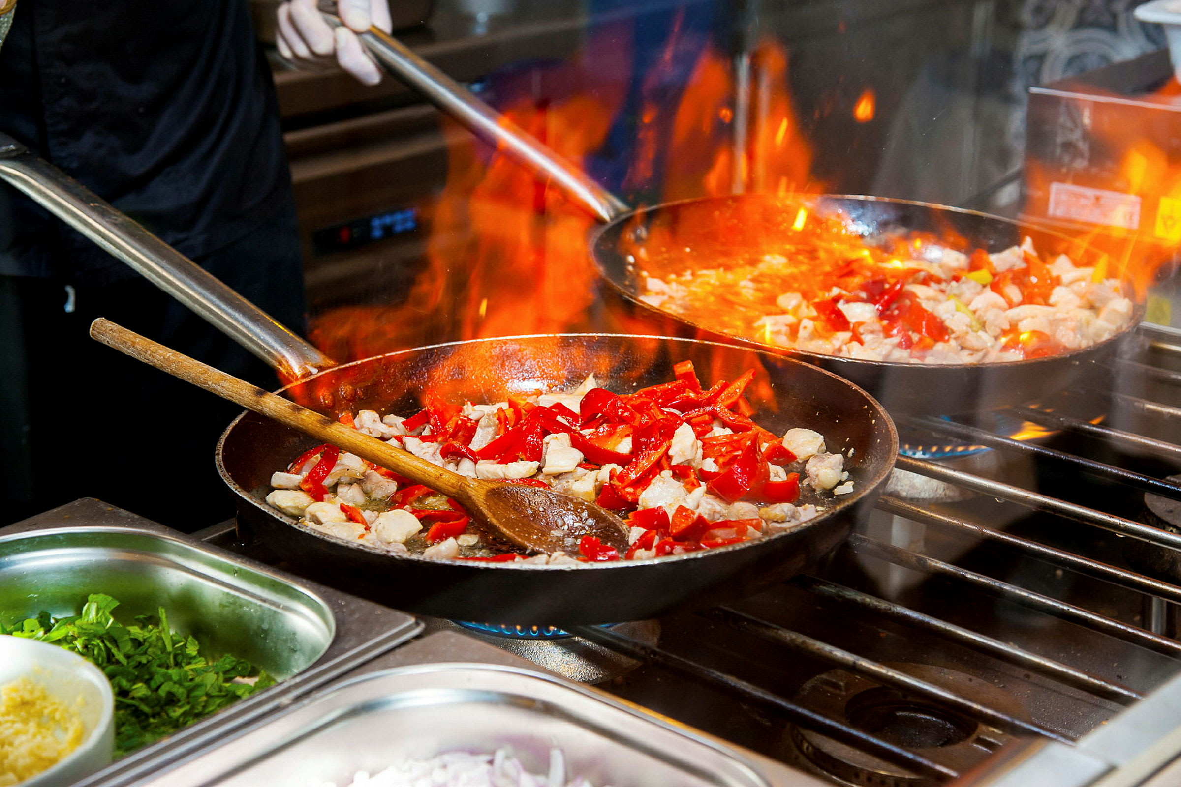 Matlaging i stekepanner med flammer, inkludert rød paprika og kylling. (AI-generert tekst)