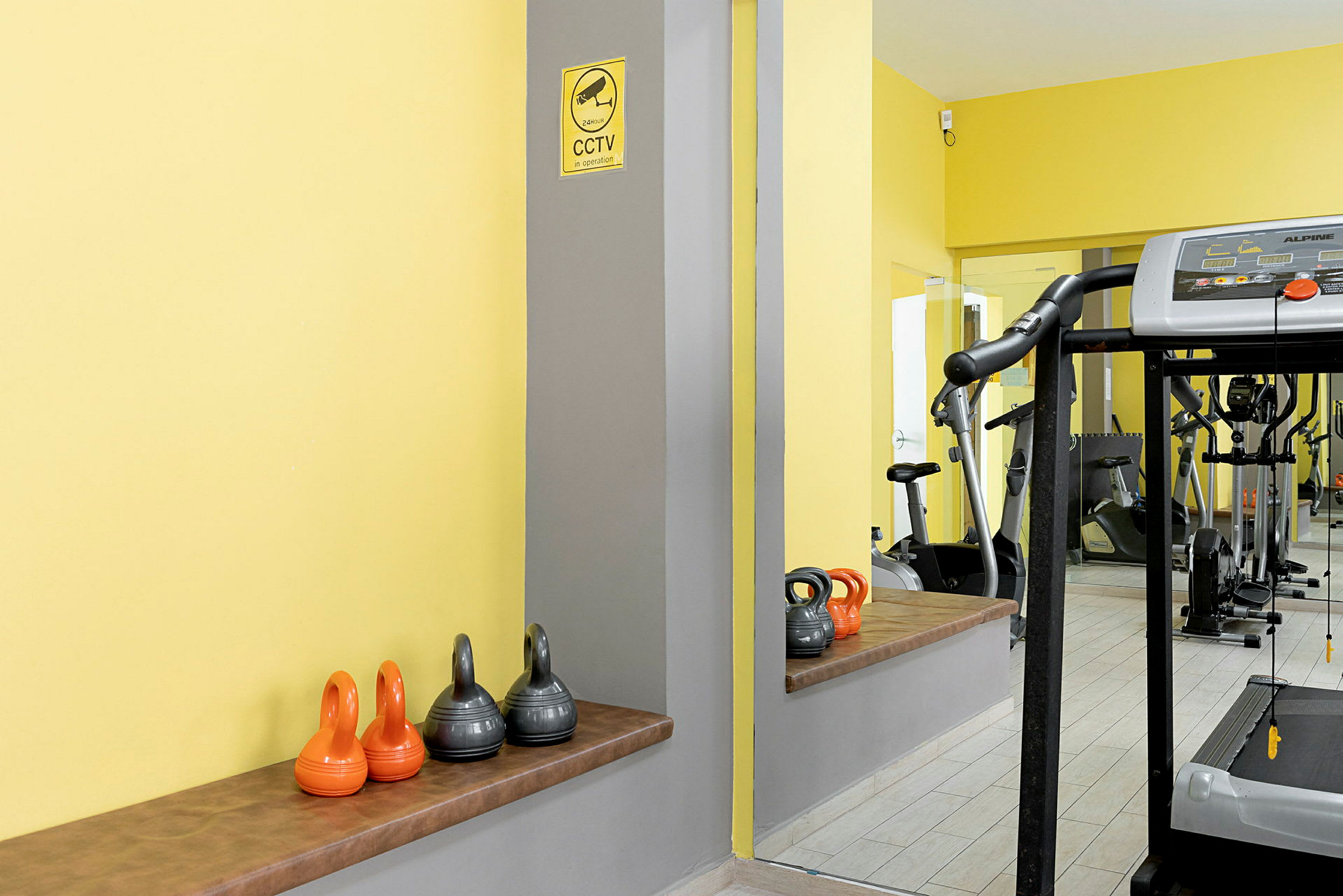 Et treningsstudio med kettlebells og en tredemølle. Veggene er malt gule. (AI-generert tekst)