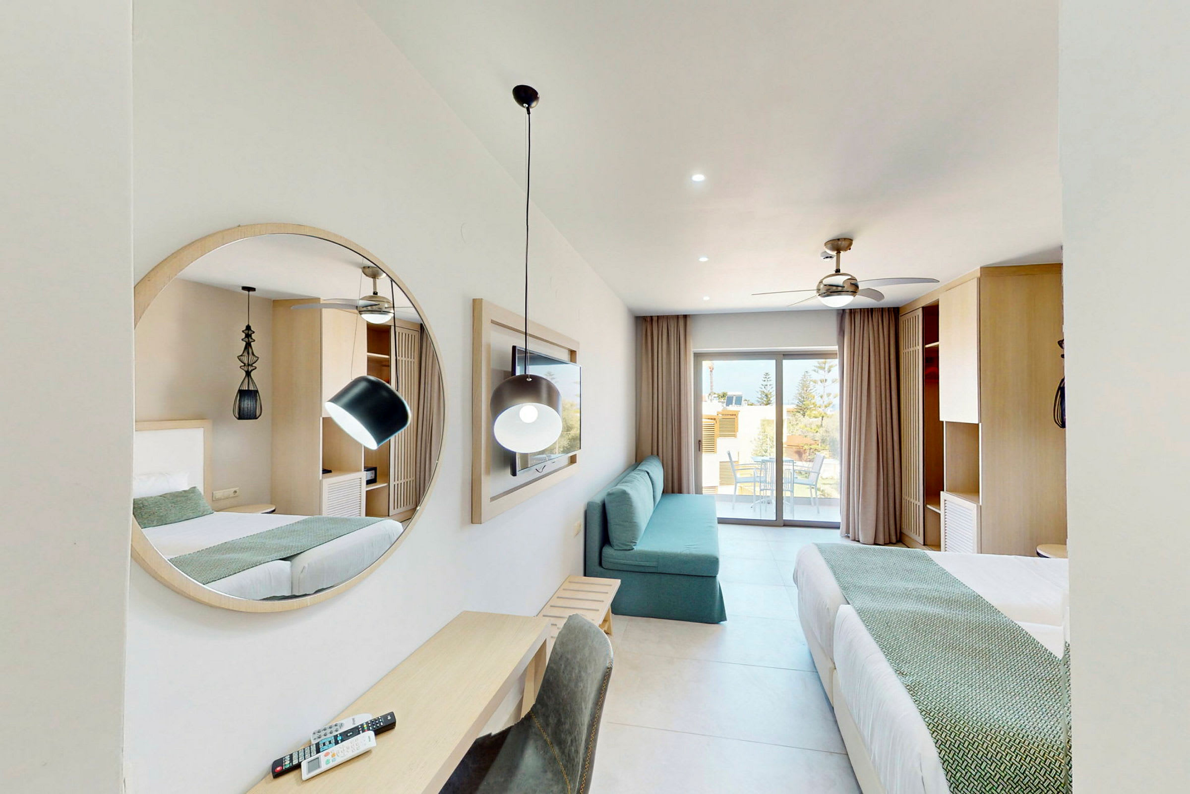Et moderne hotellrom med to senger, et speil, en sofa og et skrivebord. En balkong er synlig i bakgrunnen. (AI-generert tekst)