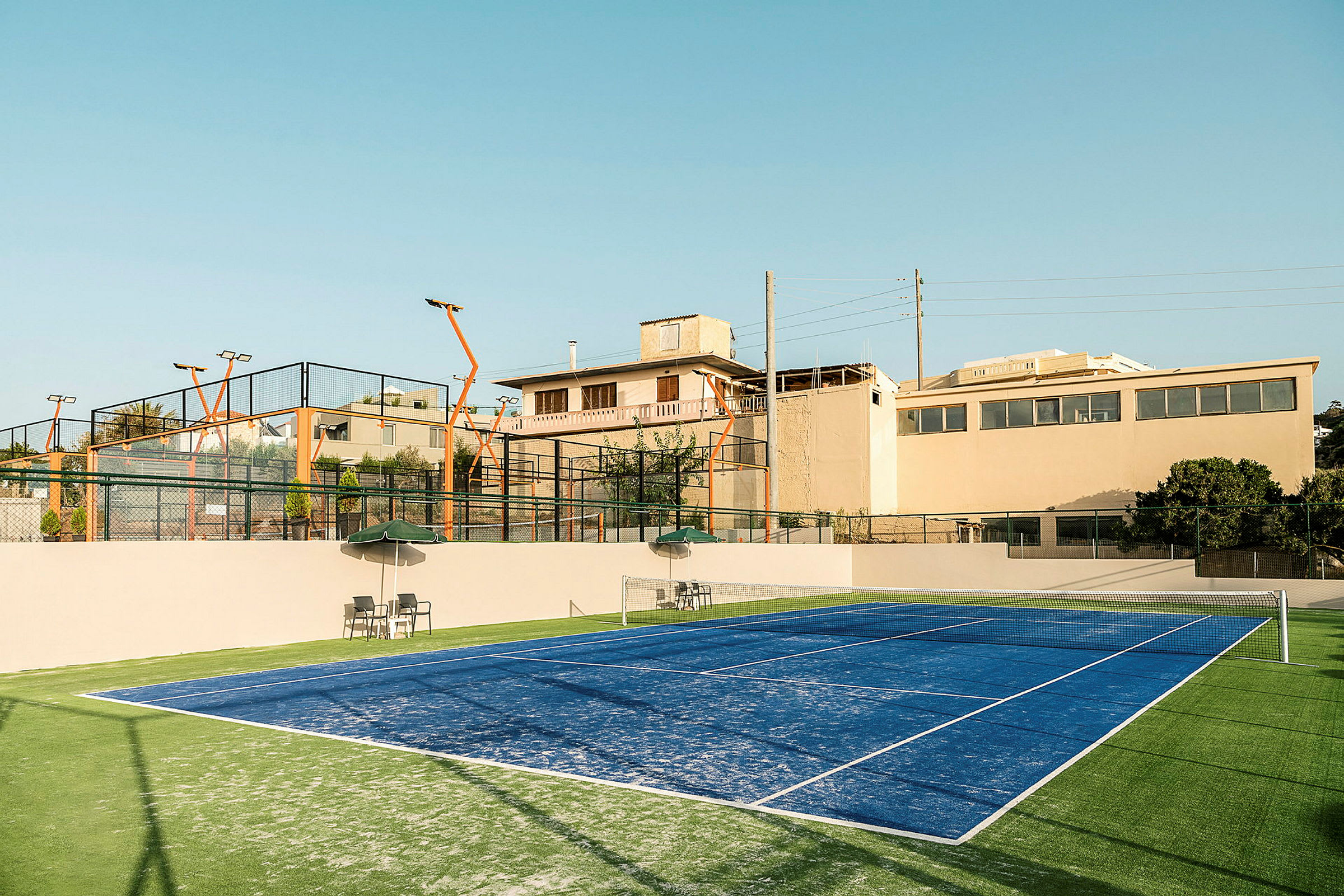 Blå padelbane med tribuner i bakgrunnen og omkringliggende bygninger. (AI-generert tekst)