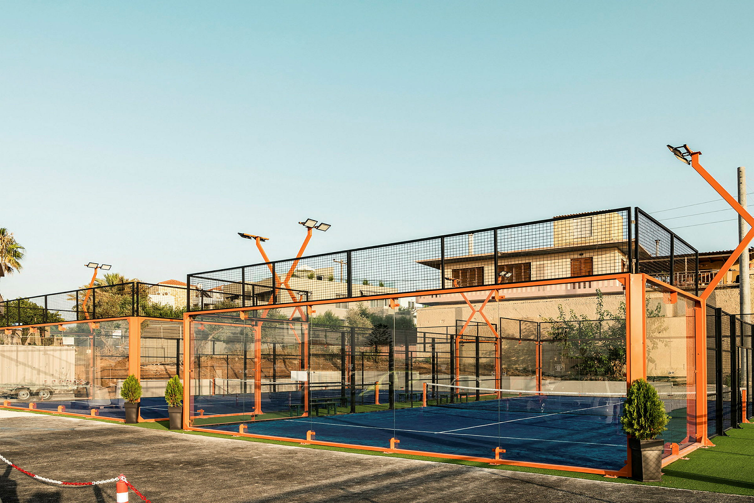 En utendørs padelbane omgitt av glass og oransje ramme. (AI-generert tekst)