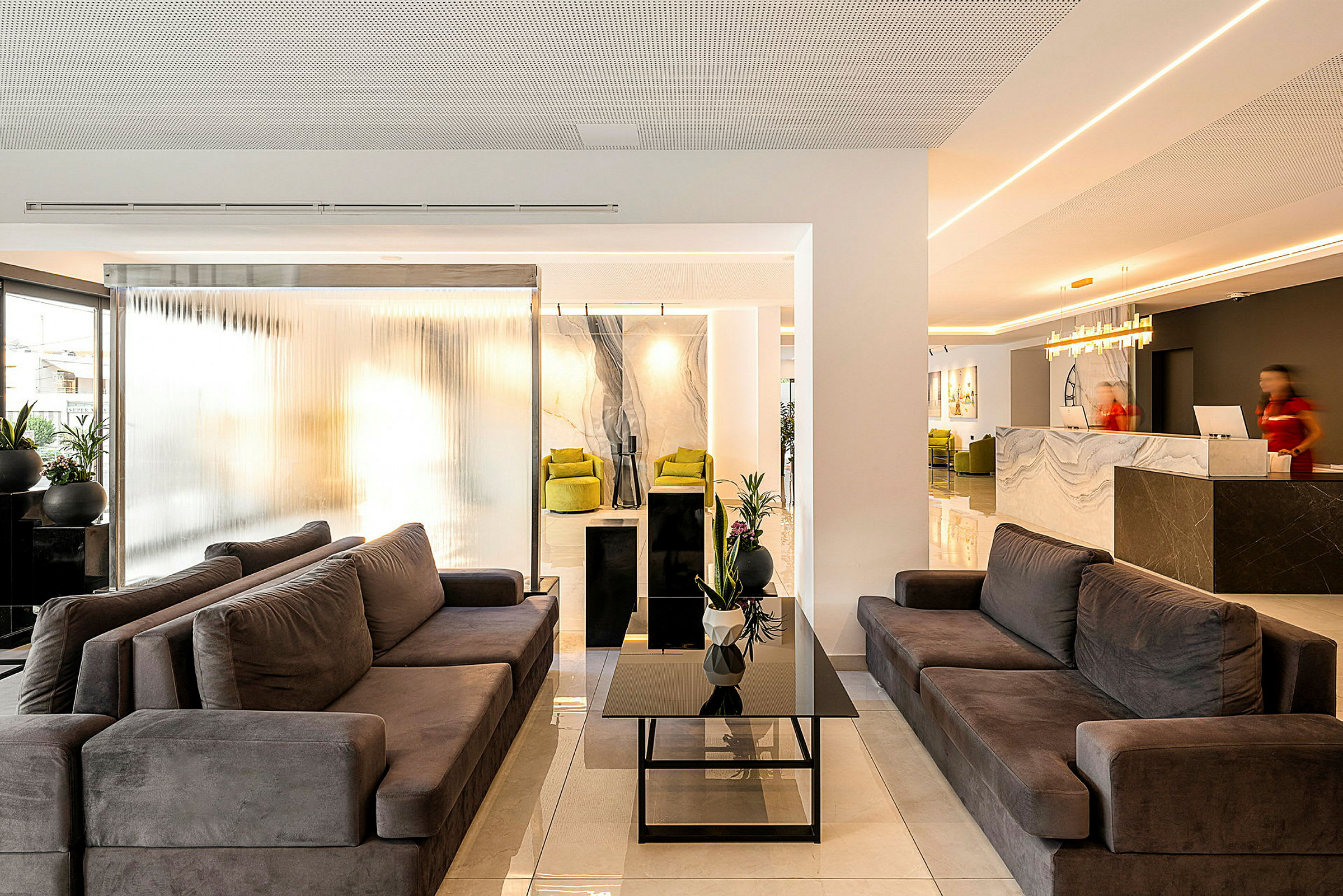 En moderne hotellobby med komfortable sofaer, et glassbord og resepsjonen i bakgrunnen. (AI-generert tekst)
