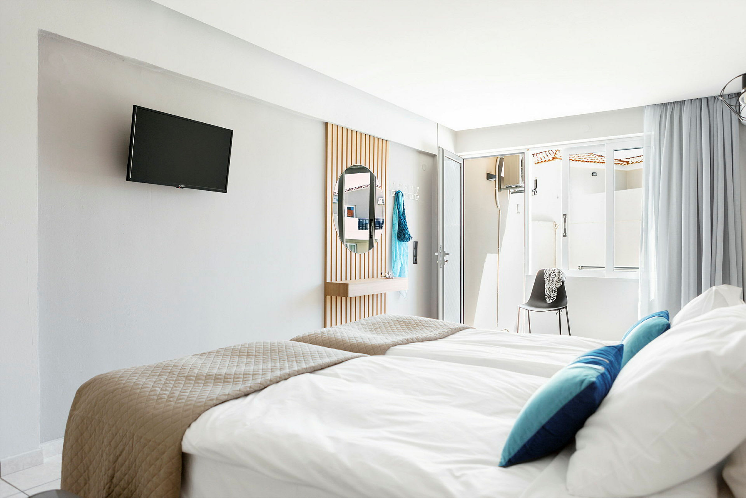 Hotellrom med senger, TV på veggen og et speil. (AI-generert tekst)
