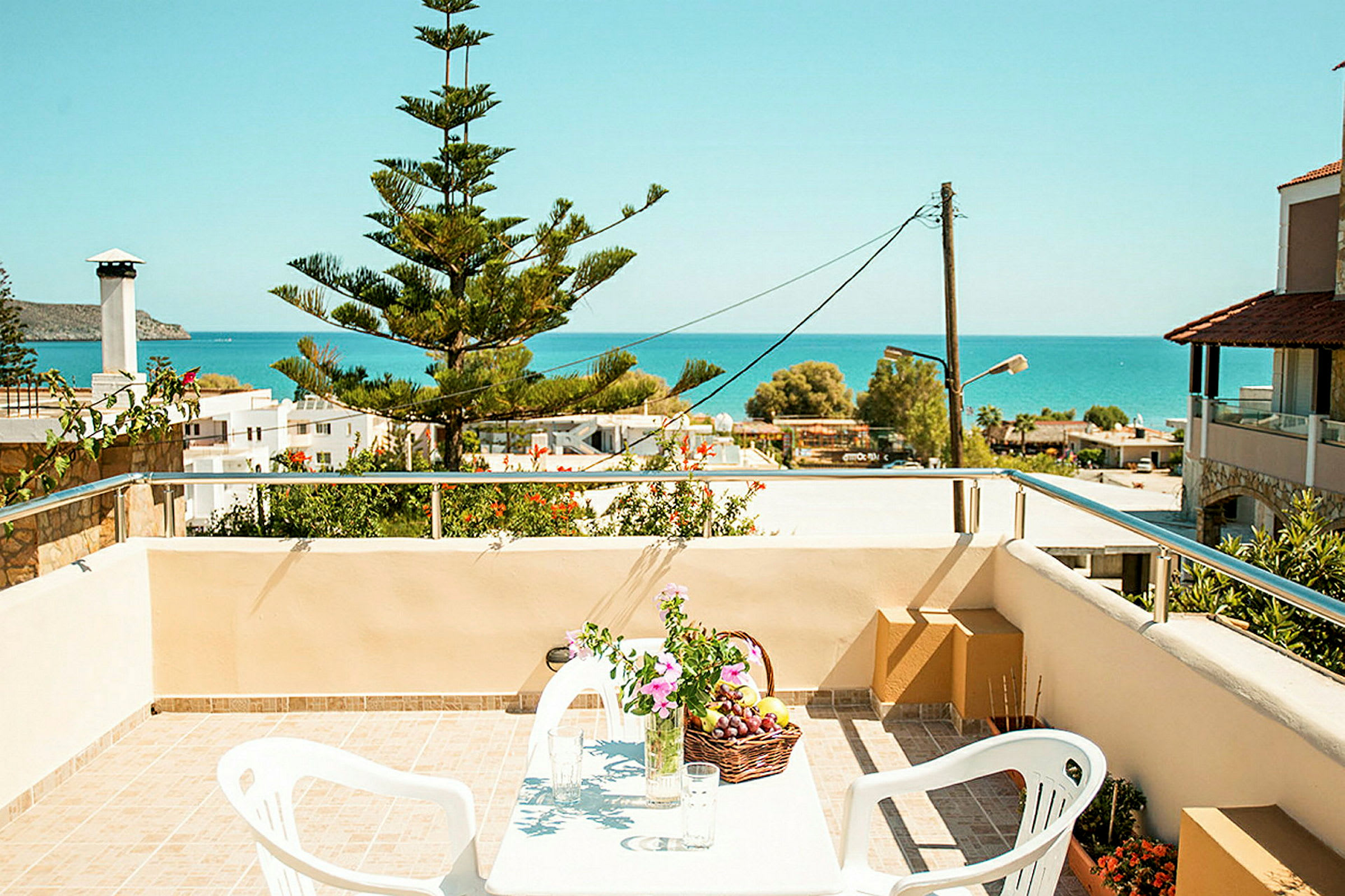 Utsikt fra en terrasse med bord, stoler og blomster, mot havet. (AI-generert tekst)