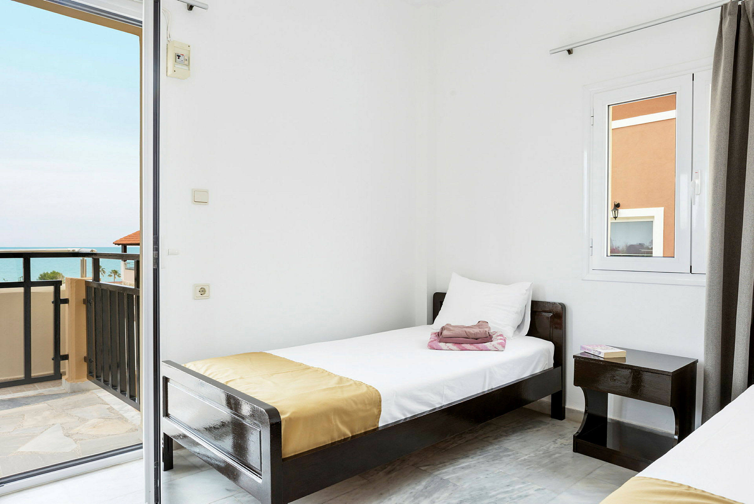 Et hotellrom med hvite vegger, en enkeltseng og en balkong med havutsikt. (AI-generert tekst)