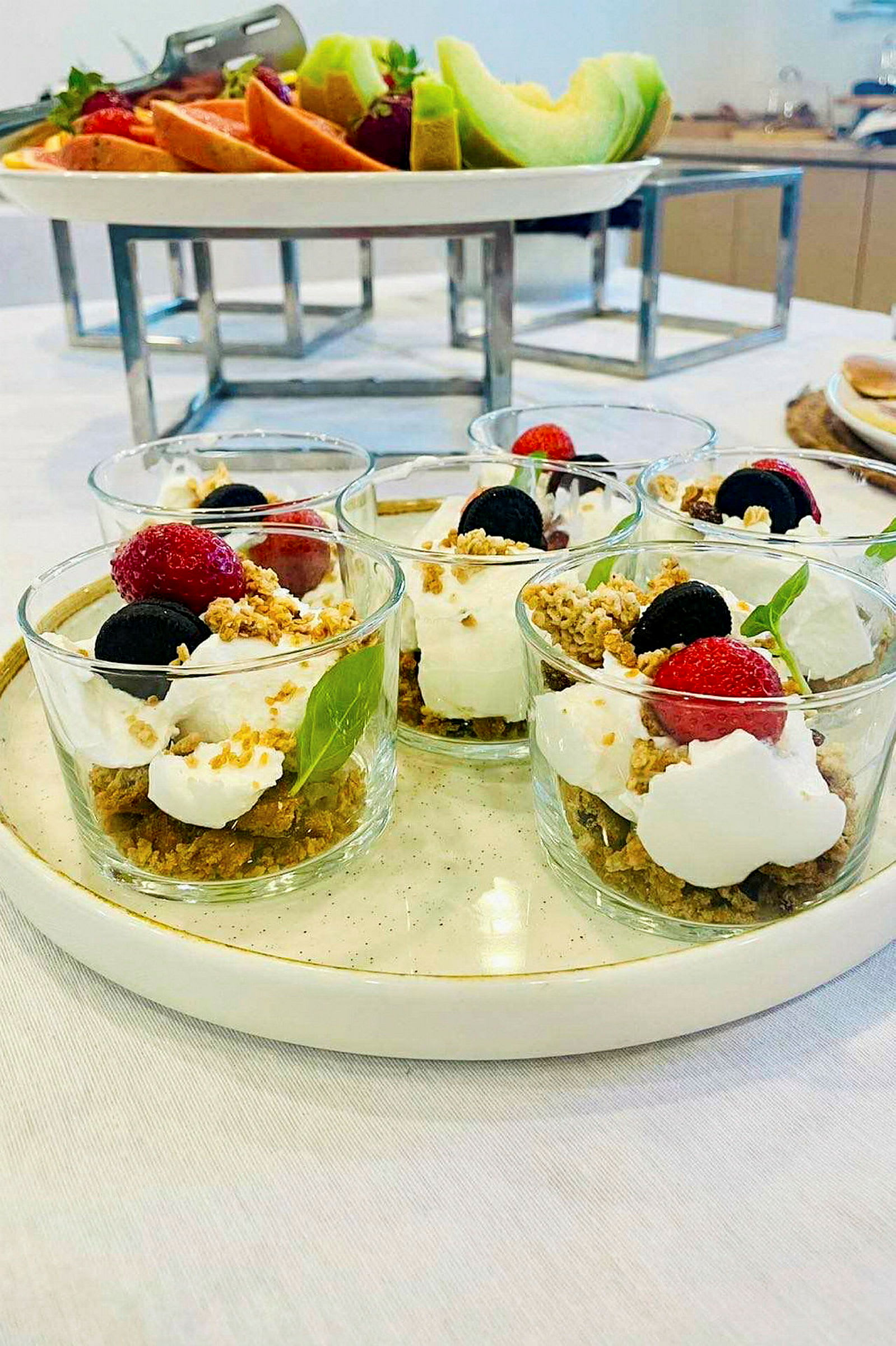 Fire glass med dessert, dekorert med friske bær og sprø topping, på en lys tallerken. (AI-generert tekst)