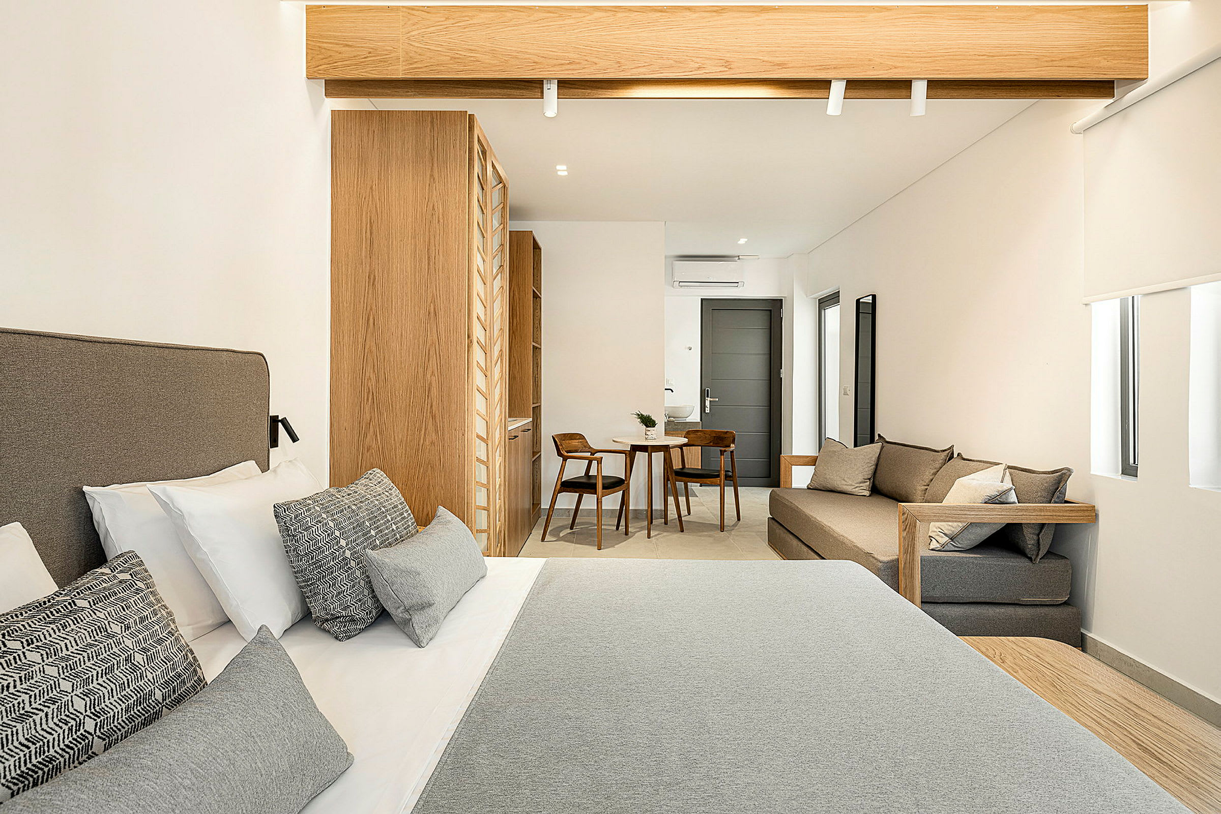 Hotellrom med en dobbeltseng i forgrunnen, treinteriør og et lite sitteområde med bord og to stoler i bakgrunnen. (AI-generert tekst)
