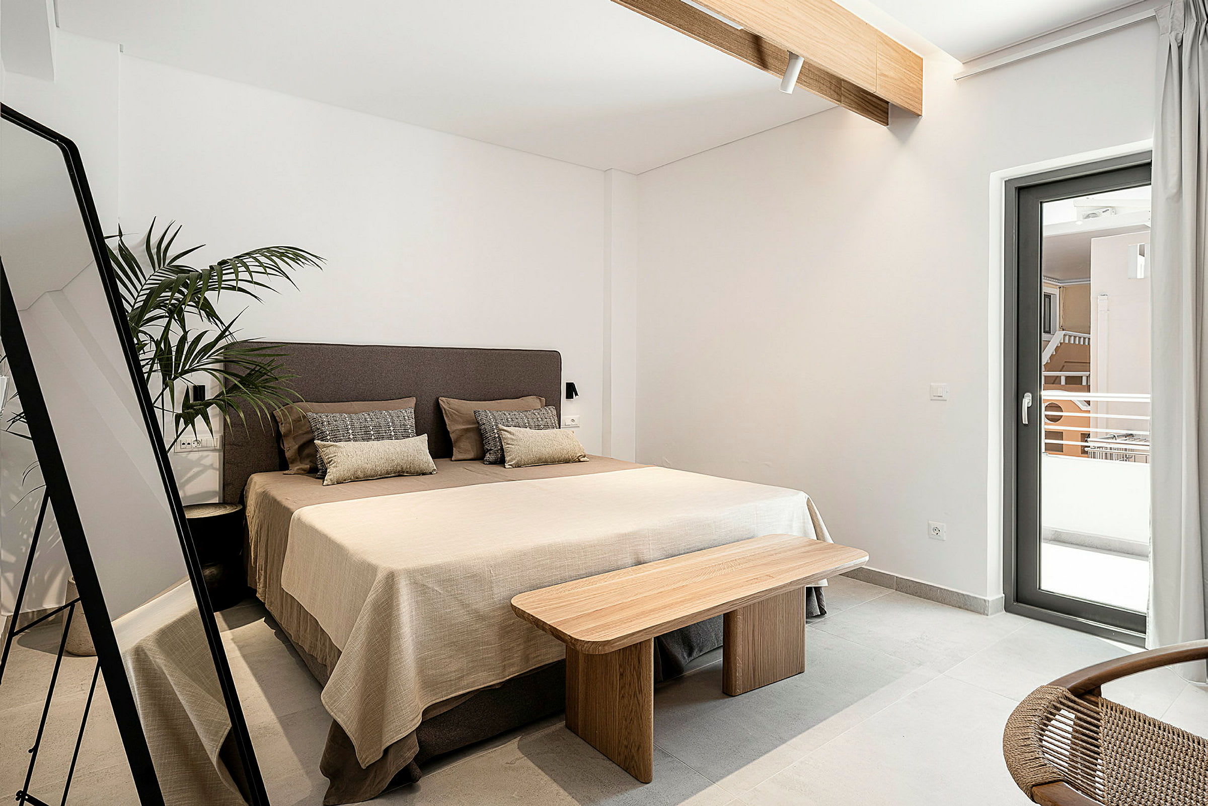 Et hotellrom med en seng, speil, plante og et vindu som vender mot en balkong. (AI-generert tekst)