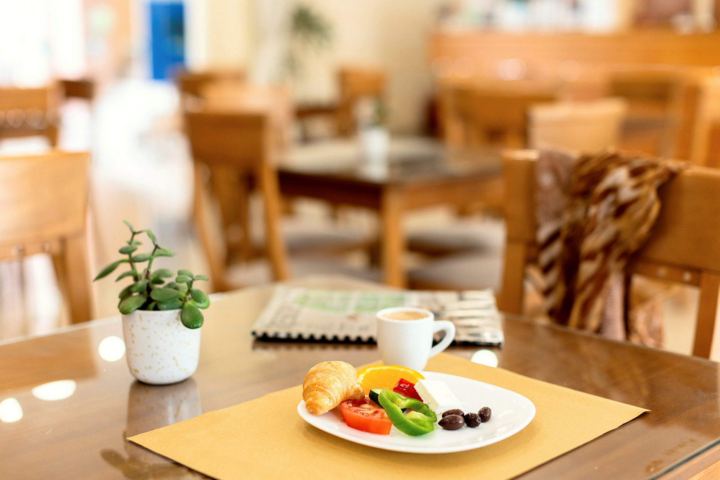 En tallerken med frokost bestående av croissant, grønnsaker og kaffe på et bord med dekorasjoner. (AI-generert tekst)