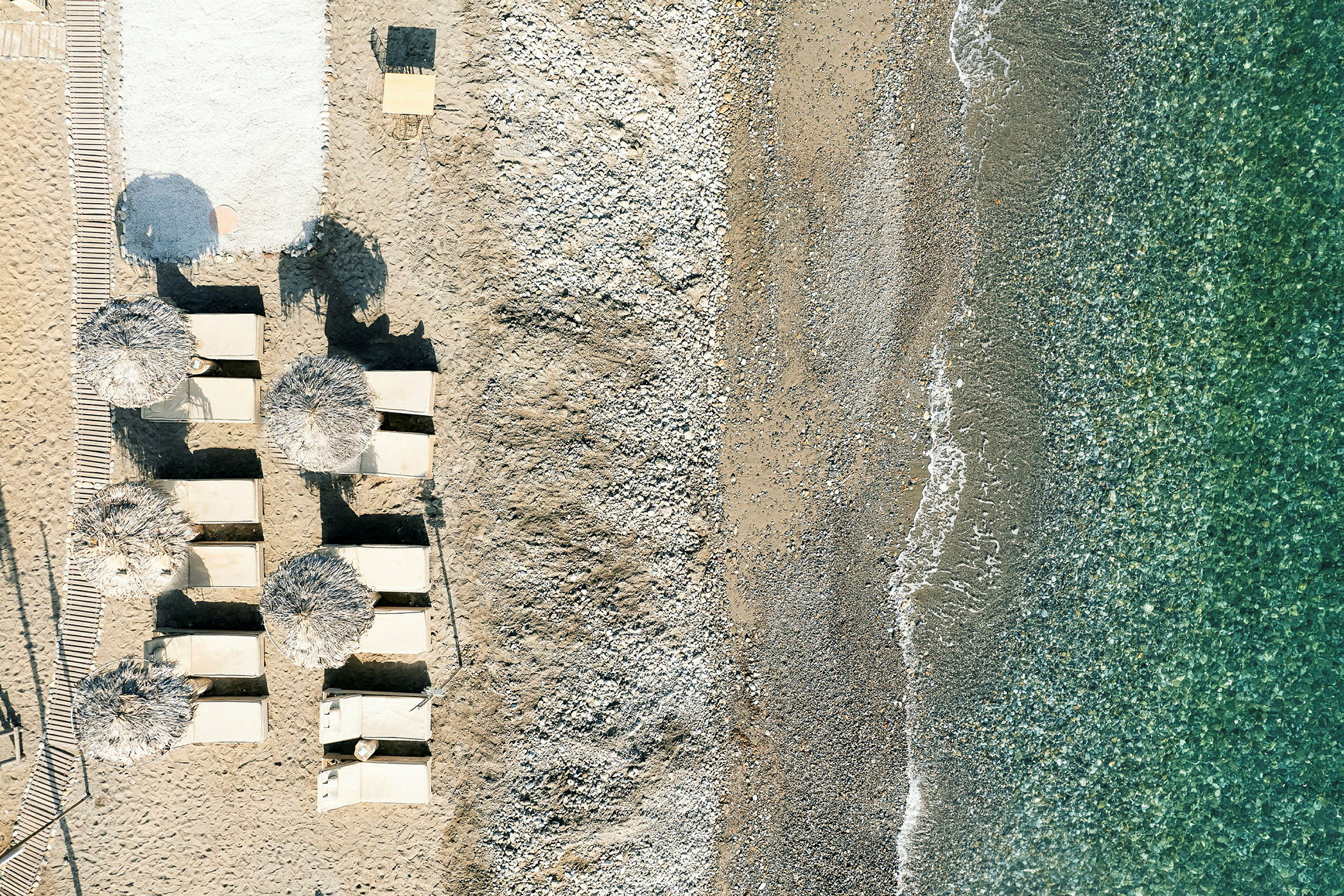 Luftfoto av en strand med solsenger og parasoller ved siden av vann. (AI-generert tekst)