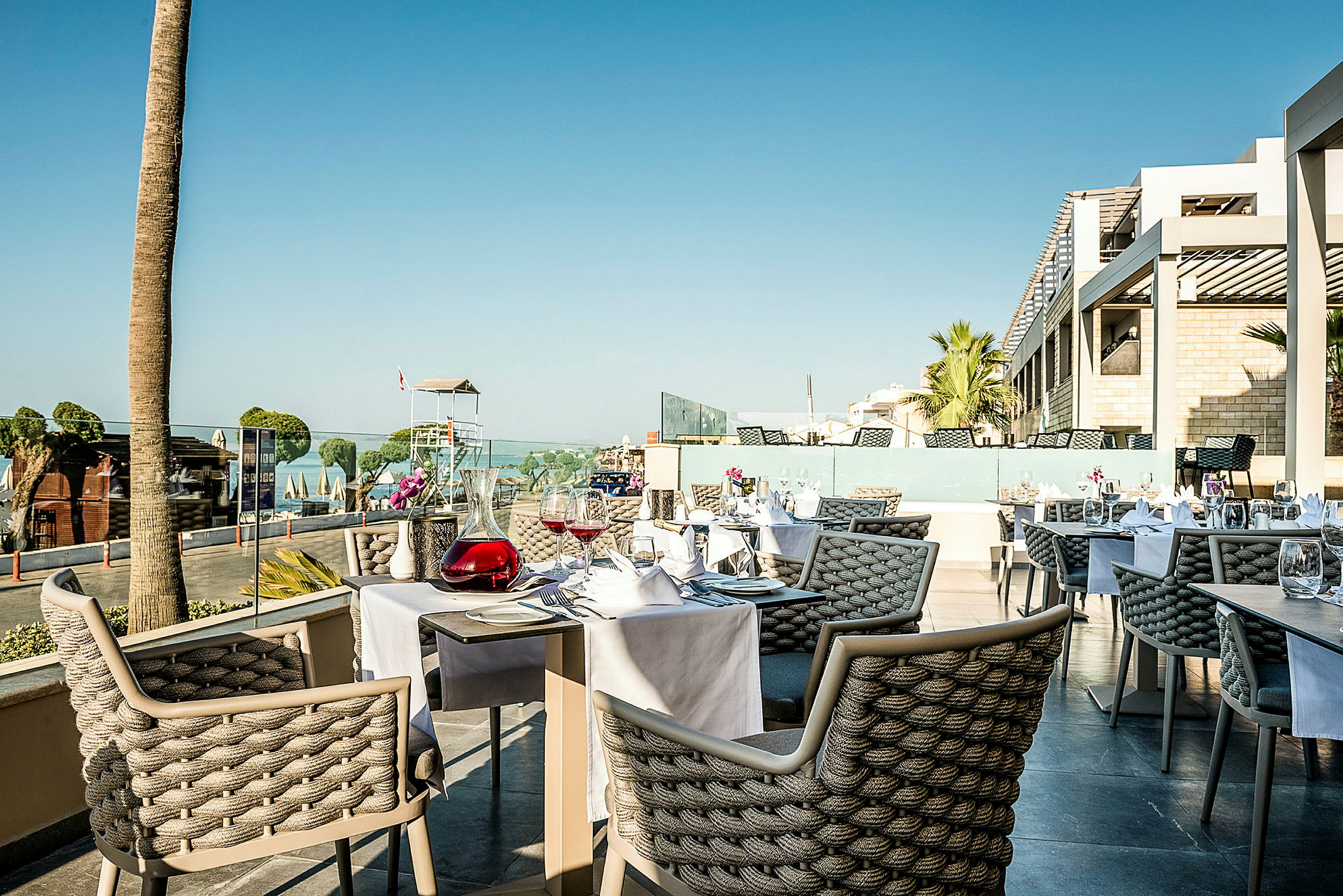 Utendørsrestaurant med dekket bord og utsikt mot strand og hav. (AI-generert tekst)