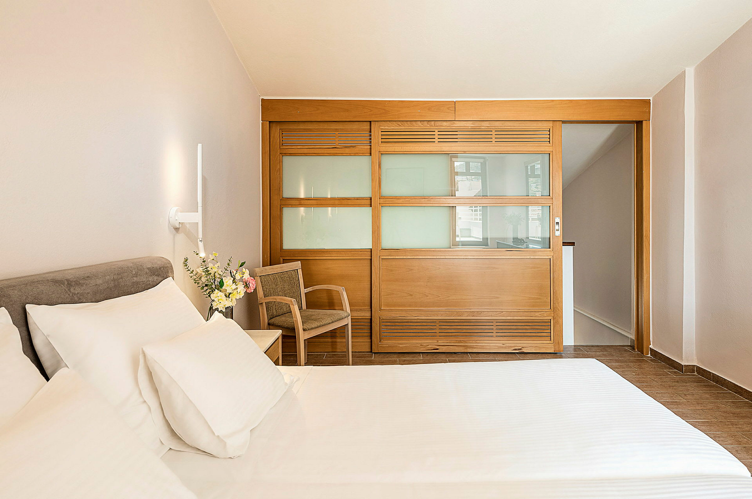 Hotellrom med seng, stol og en trepanel med glass. (AI-generert tekst)