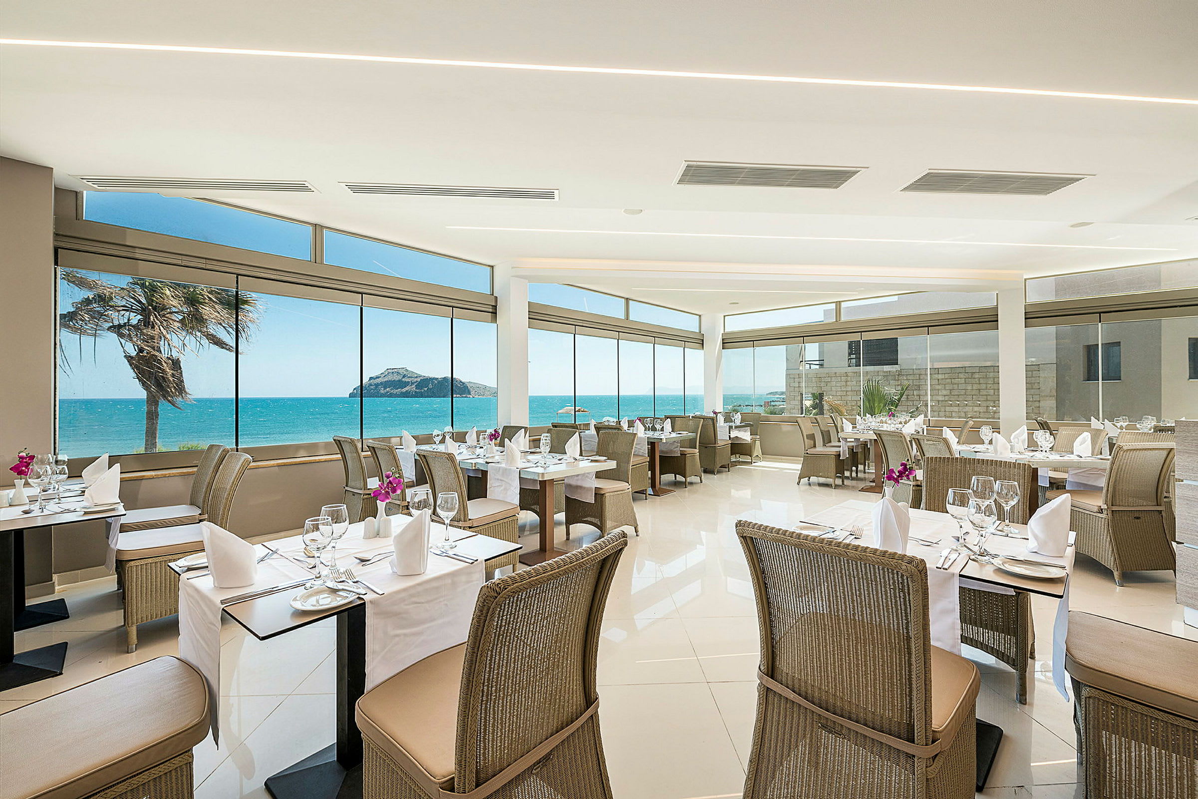 Restaurant med utsikt mot havet, dekkede bord og rottingstoler. (AI-generert tekst)