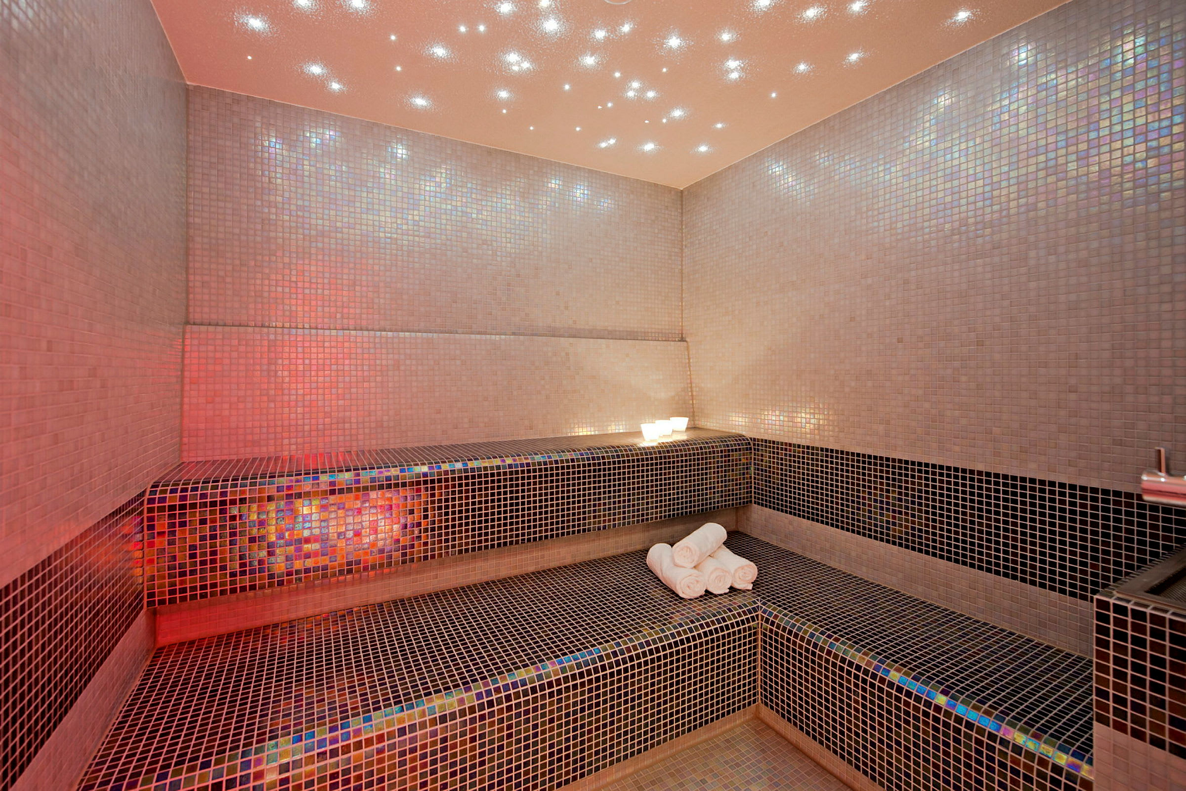 Rommet er et mosaikkflislagt spa med en benk og håndklær. (AI-generert tekst)