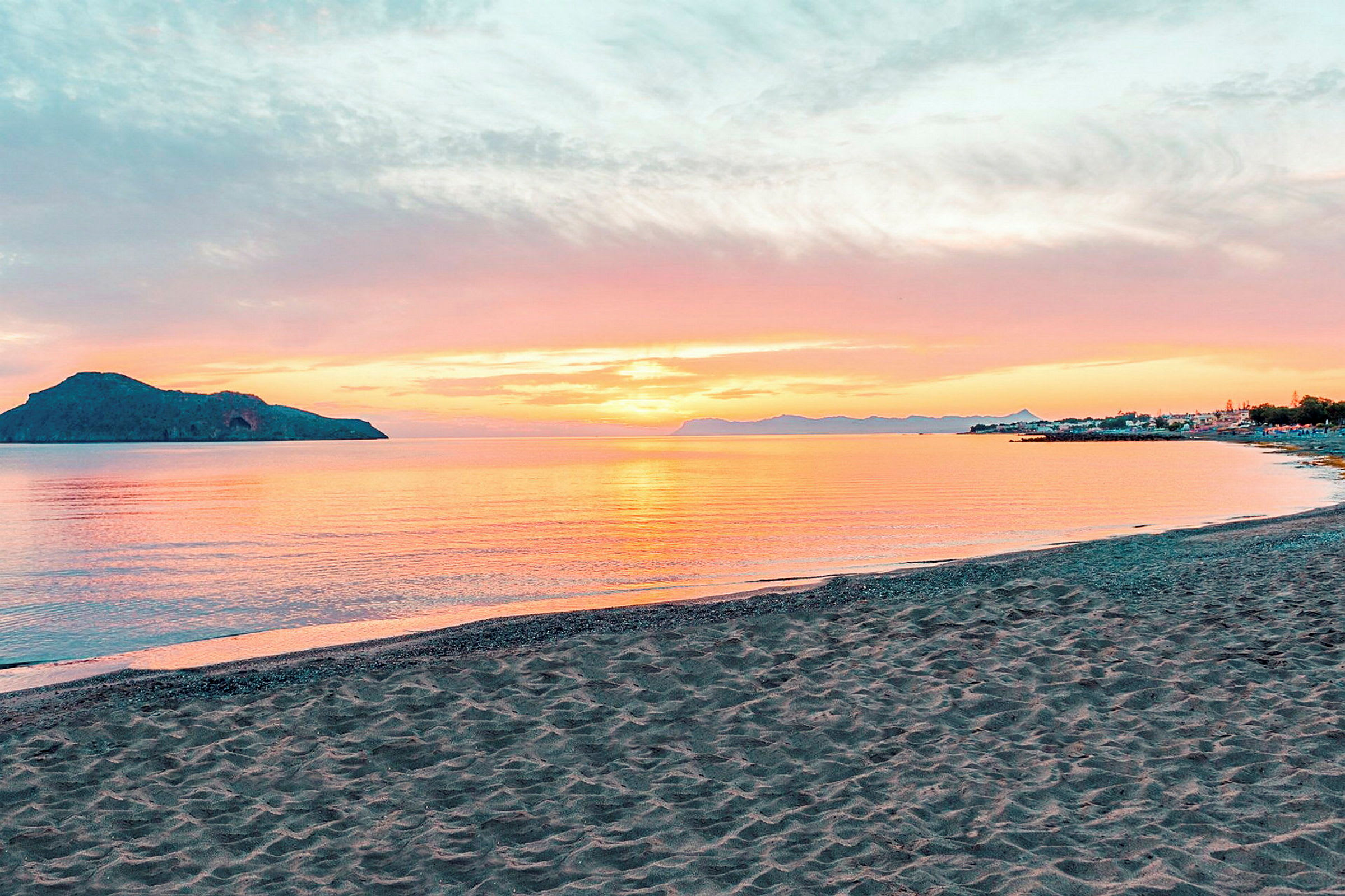 En strand med gyllen sand foran et stille vann ved solnedgang. (AI-generert tekst)