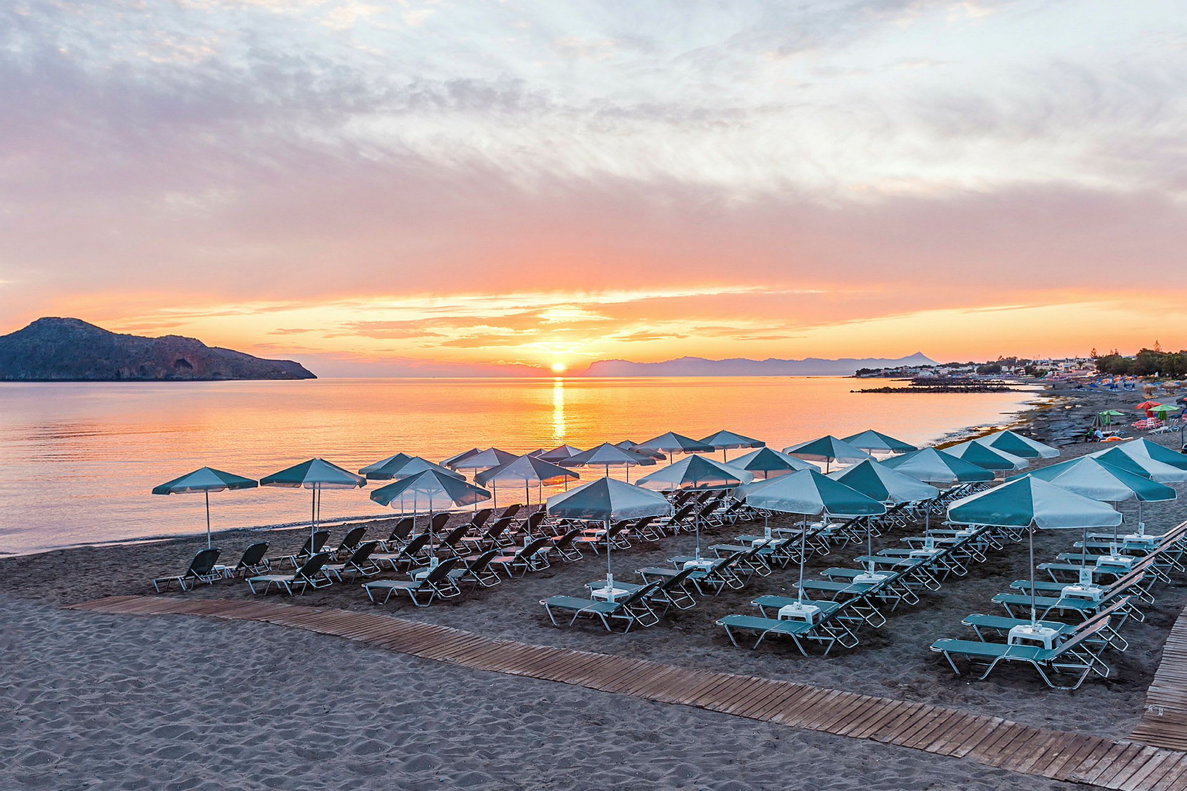 Strand med solsenger og parasoller ved solnedgang. (AI-generert tekst)