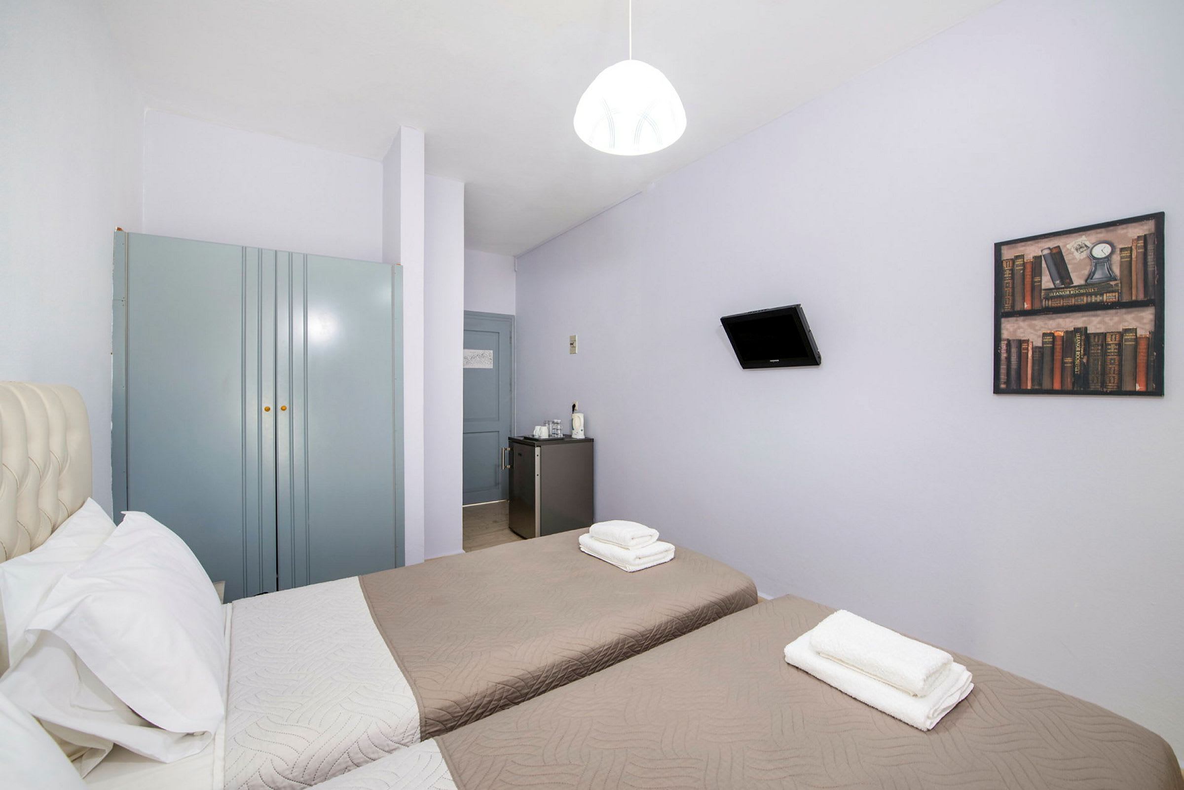 Hotellrom med to enkeltsenger, et garderobeskap, et lite kjøleskap og en veggmontert TV. (AI-generert tekst)