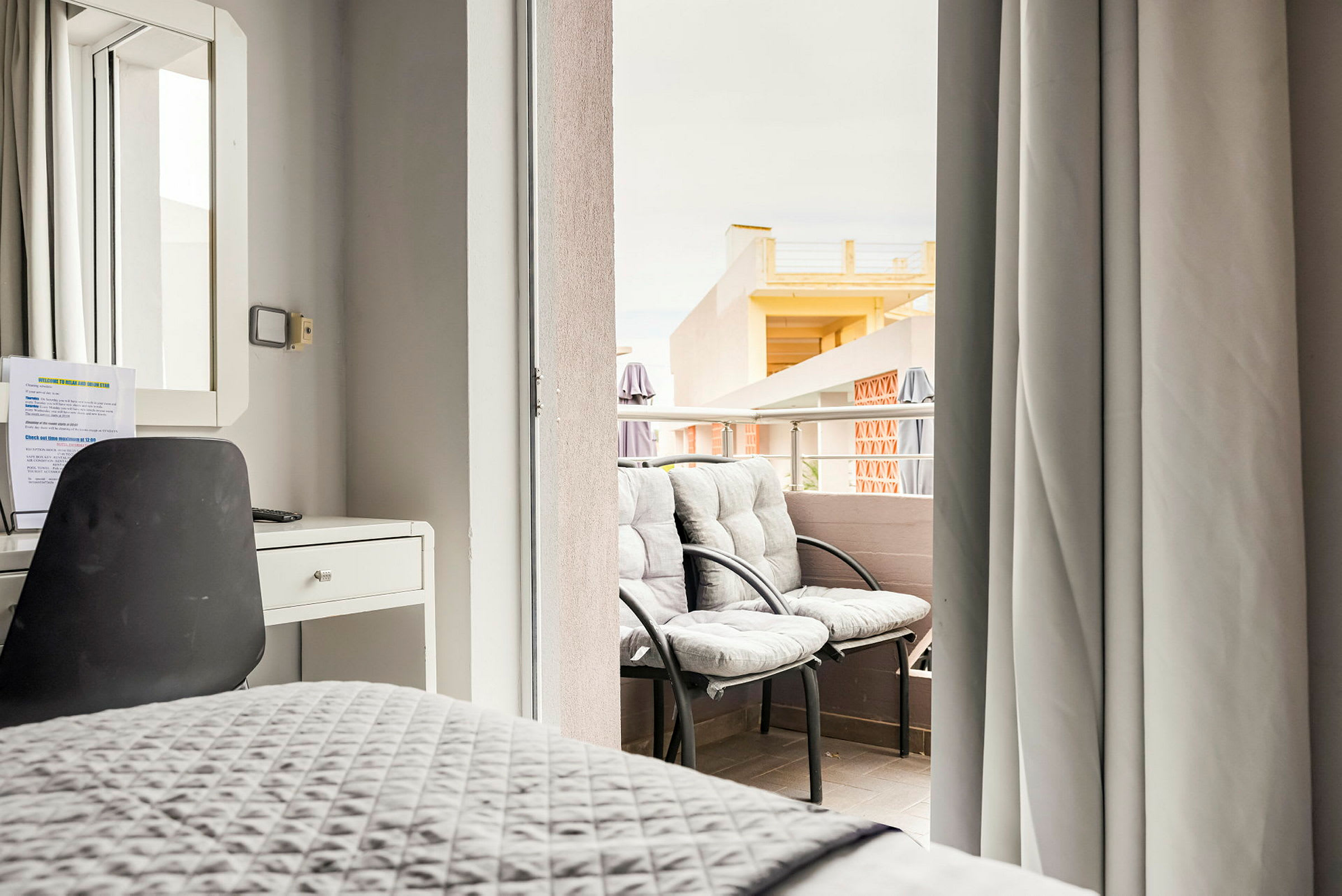 Et hotellrominnredning med skrivebord og stol og utsikt over en balkong med to stoler. (AI-generert tekst)
