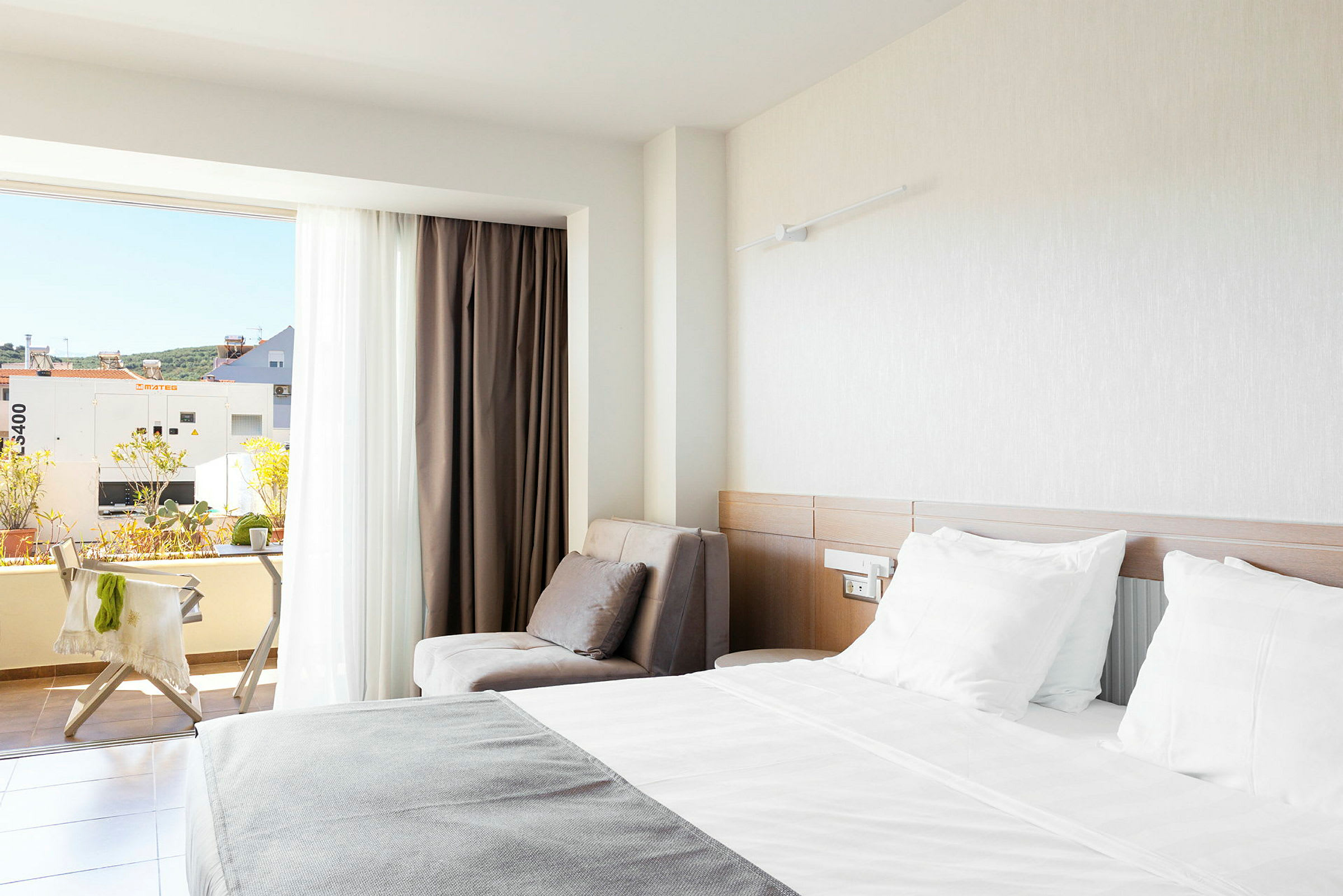 Et hotellrom med en dobbeltseng, en lenestol og en balkong med utsikt. (AI-generert tekst)
