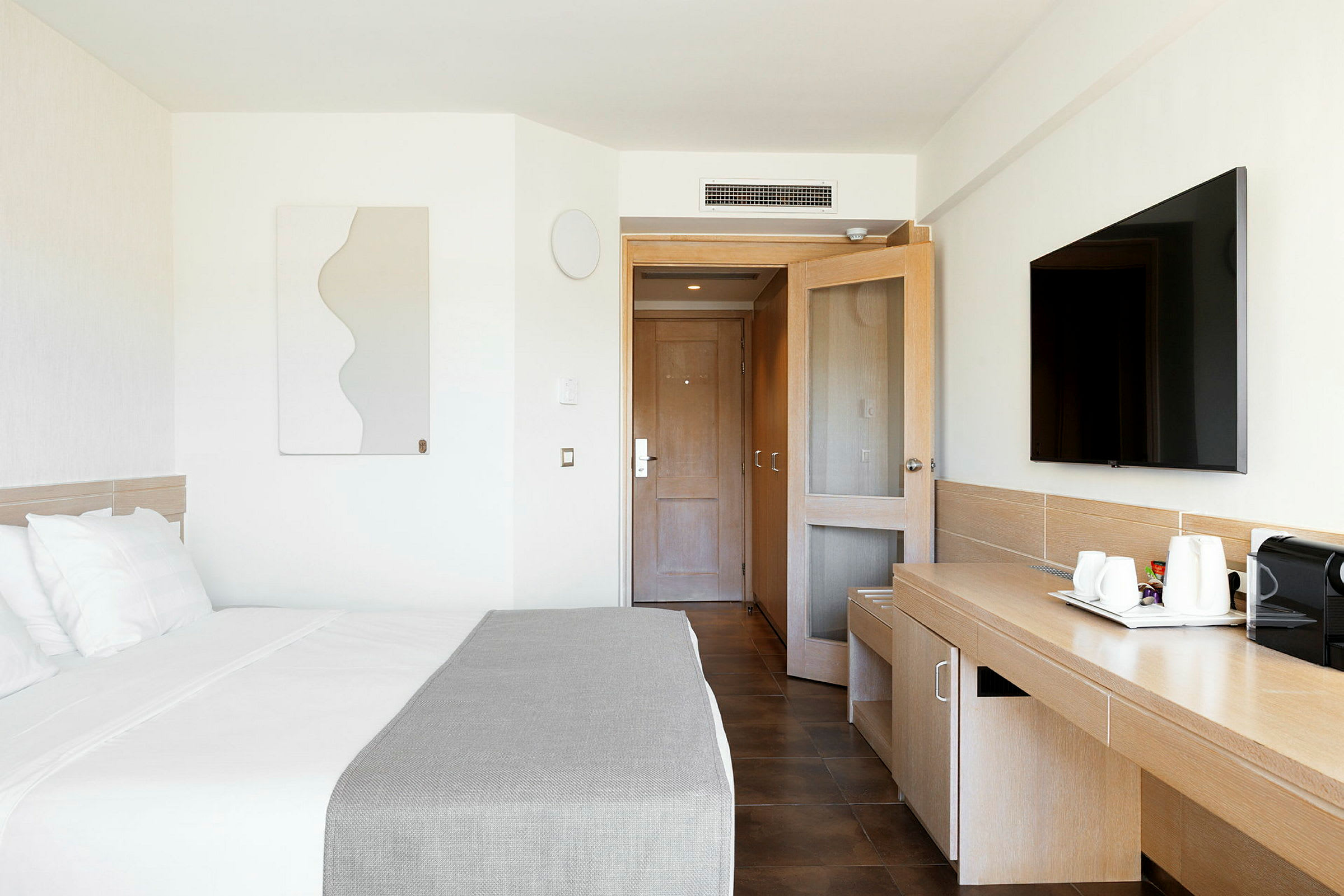 Et moderne hotellrom med en seng, et skrivebord, en TV og en dør i bakgrunnen. (AI-generert tekst)