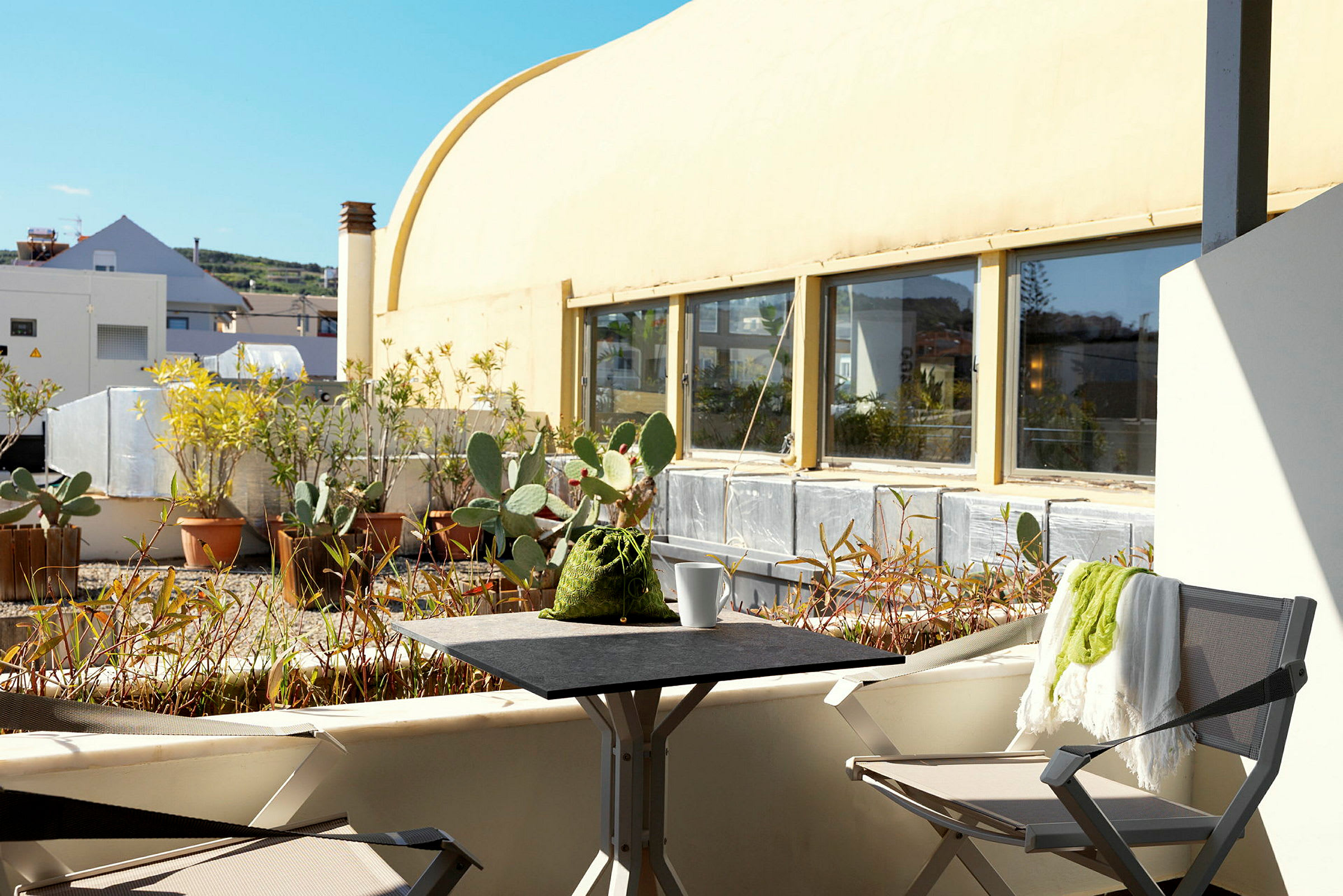 En solrik terrasse med stoler, bord og planter i potter. (AI-generert tekst)